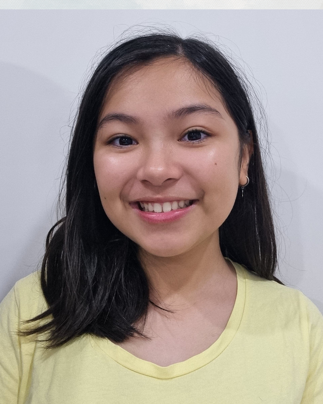 A young woman with shoulder-length dark hair, wearing a yellow top, smiling against a white background.