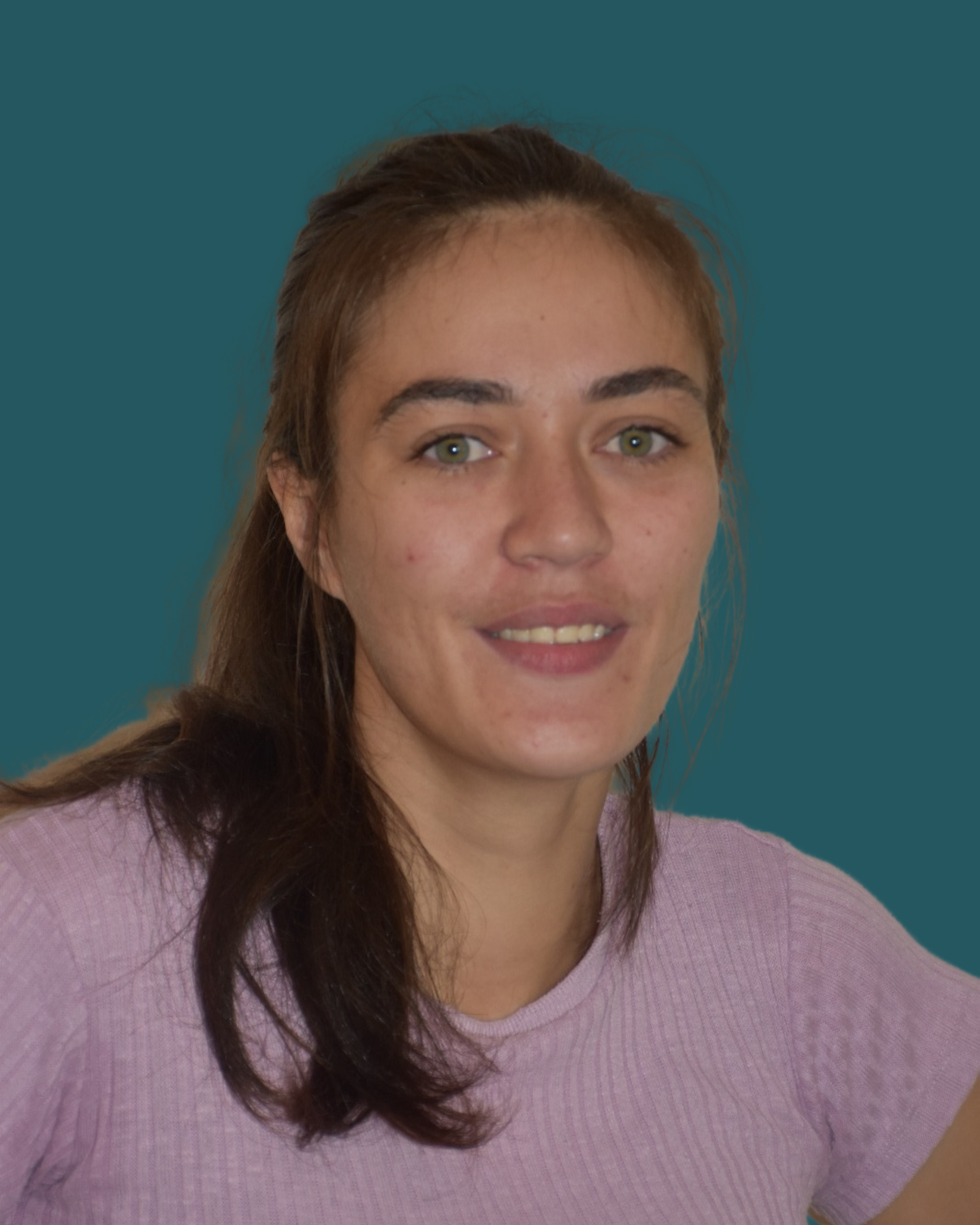 A young woman with brown hair, green eyes, wearing a pink shirt, smiling, short background.