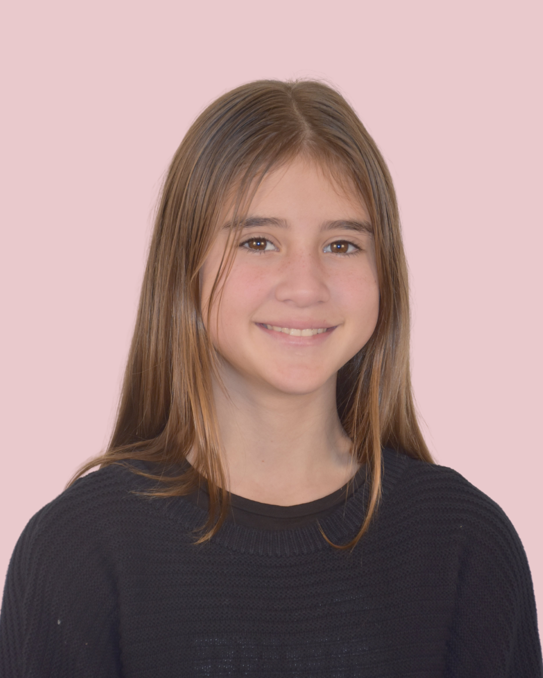 Portrait of a young woman with long brown hair, wearing a black sweater, smiling, against a pink background.