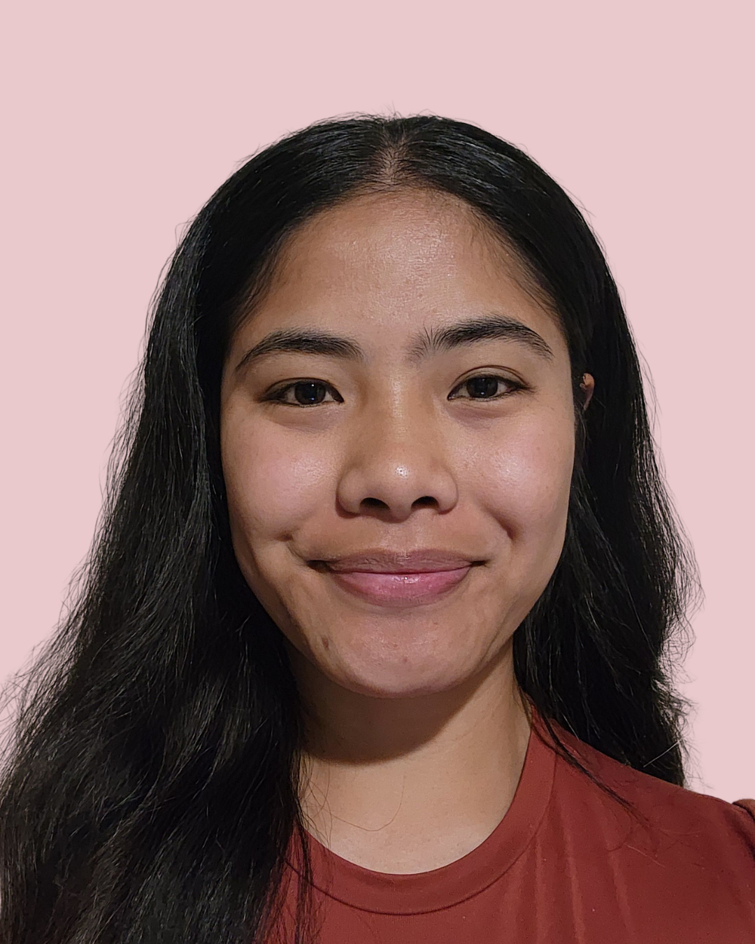 Close-up photo of a smiling young Asian woman with long black hair, wearing a reddish-brown shirt, against a light pink background.