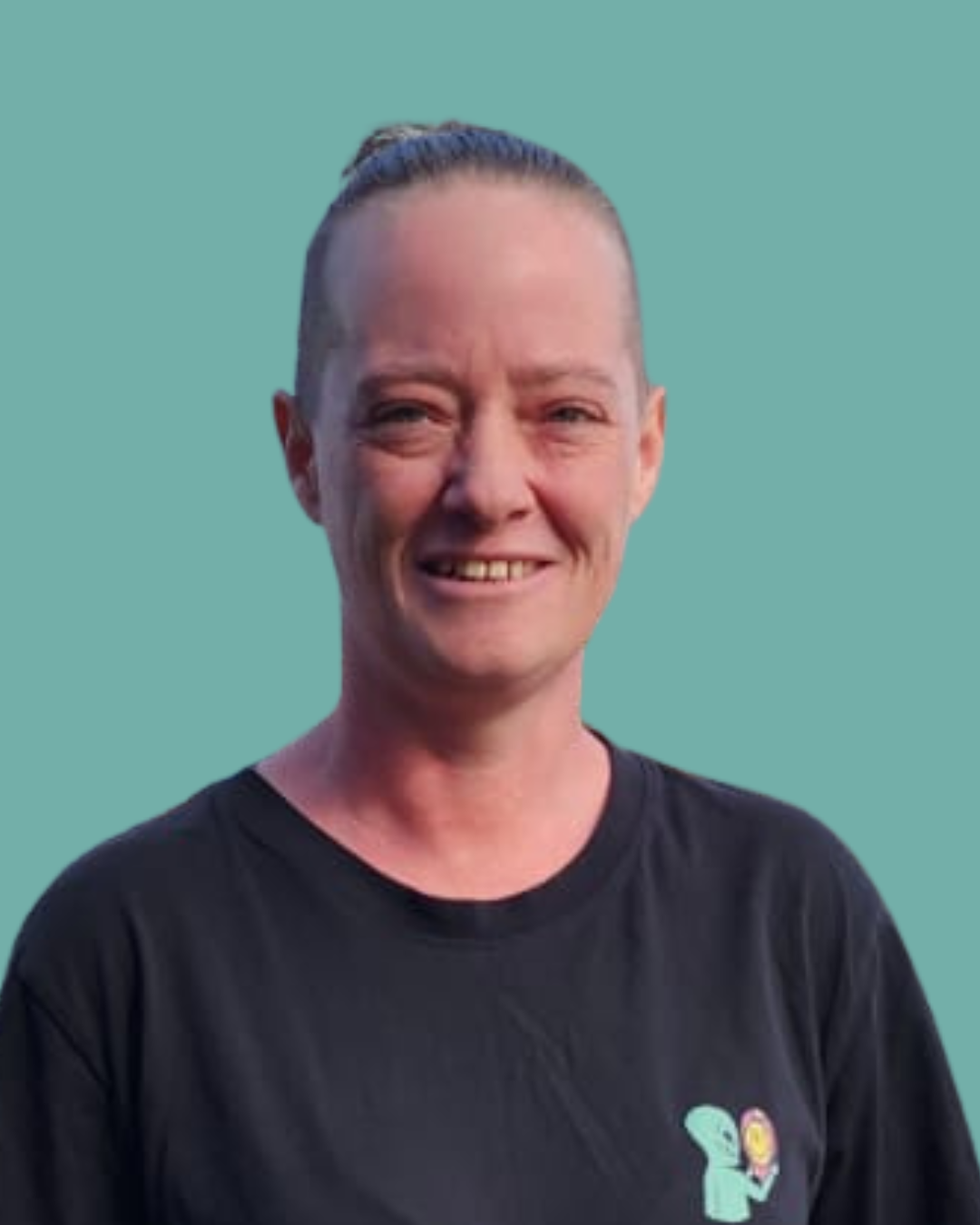 A woman with light skin and dark hair styled in a bun, wearing a black T-shirt with a small logo on the chest, smiling against a solid teal background.