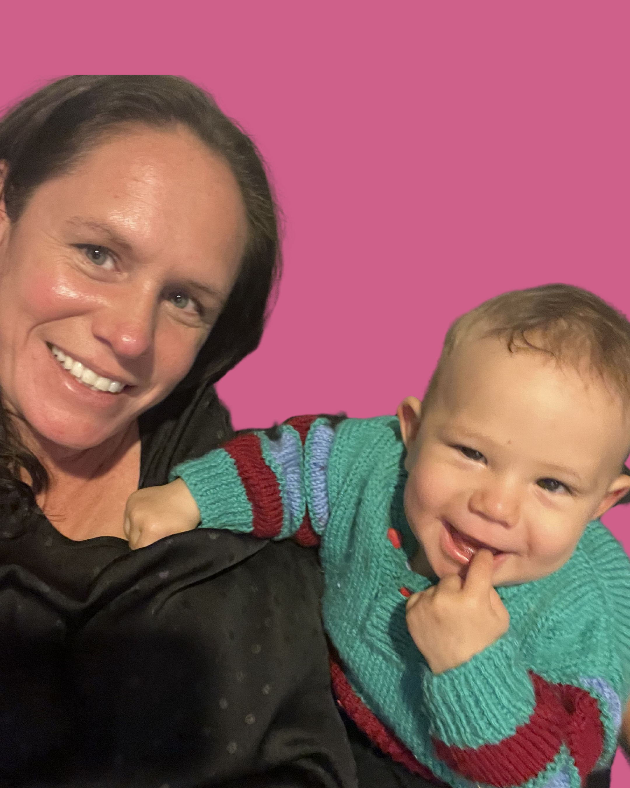 A woman with brown hair smiling next to a young boy with light brown hair, wearing a colorful sweater, smiling and touching his lips.