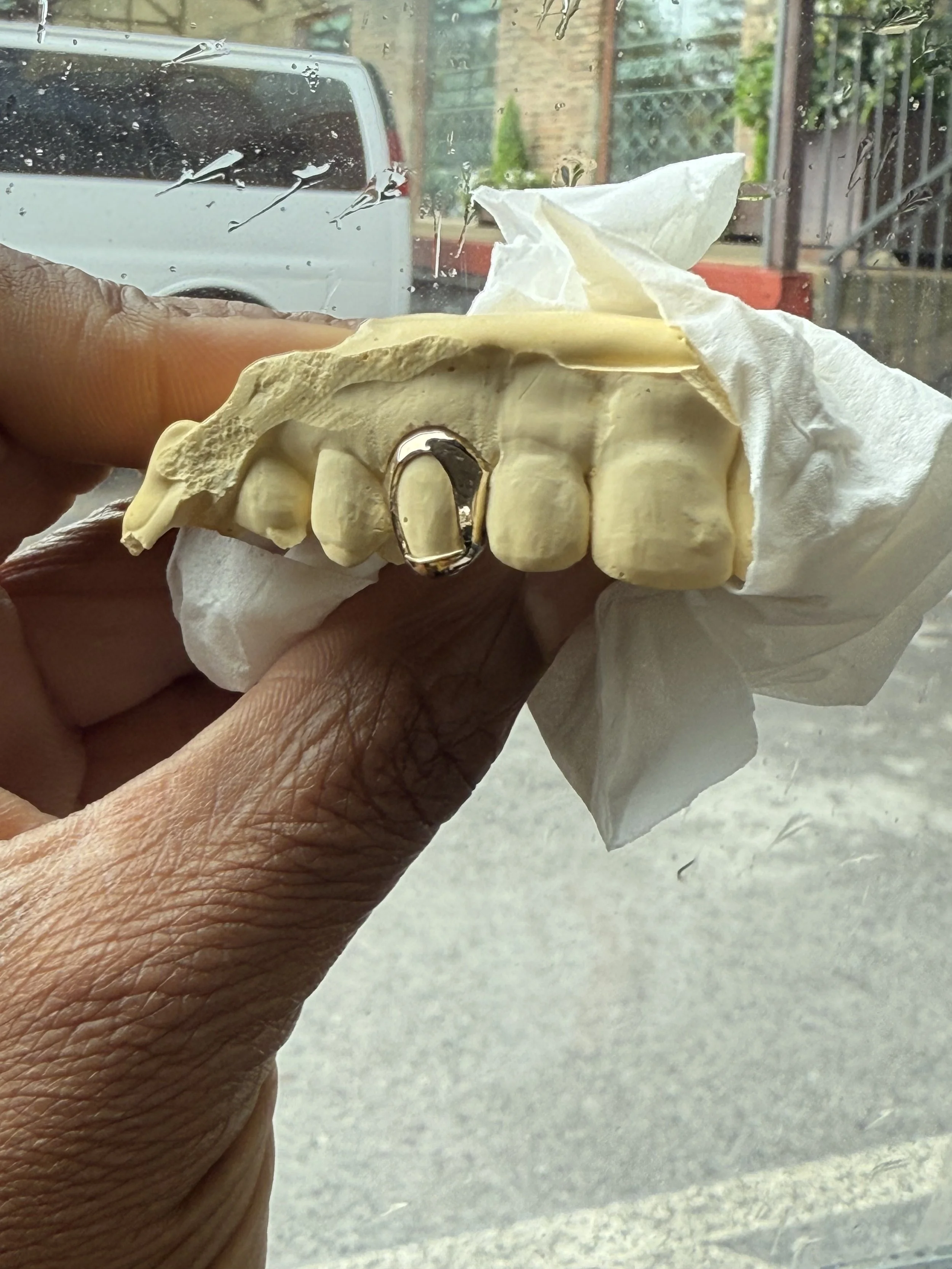 A hand holding a dental model or mold with a gold grillz  in the front on the south side of Chicago.