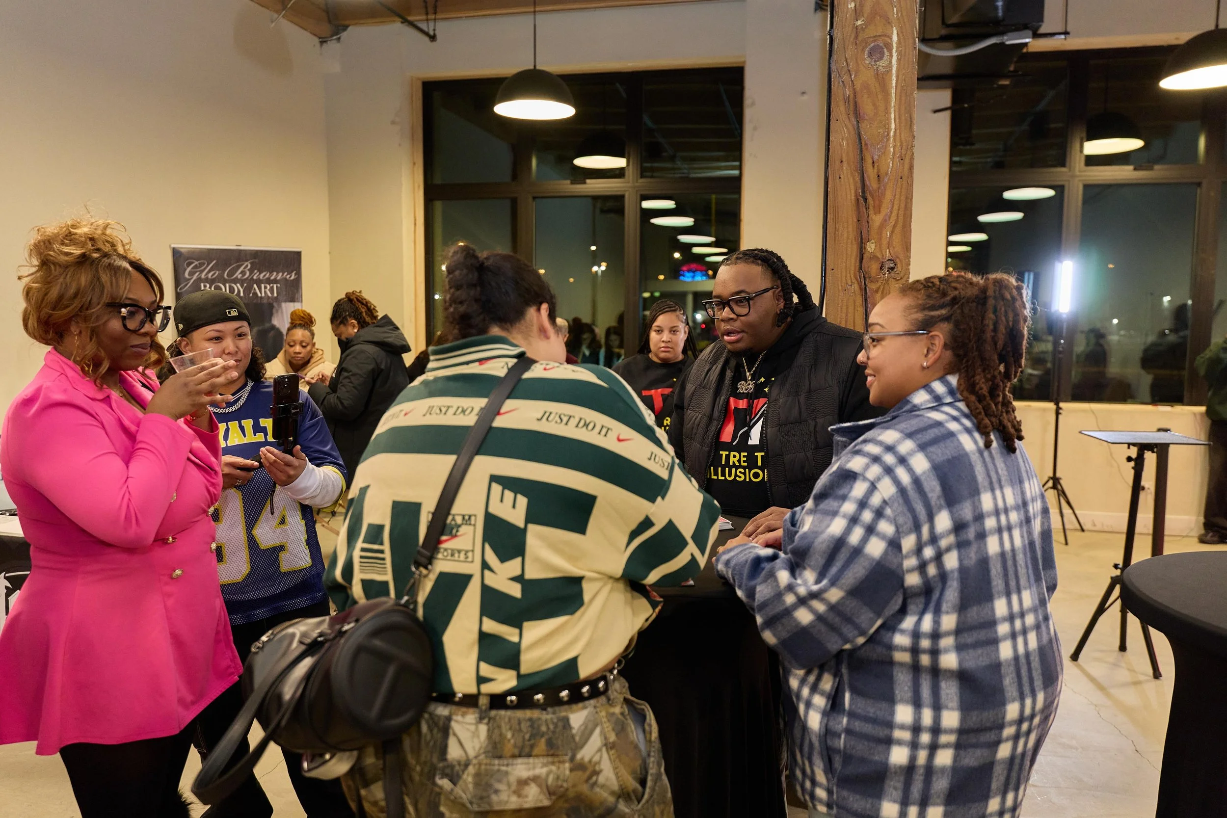 A group of people gathered around a table at an indoor event, engaging in conversation at Jem Junkies Tooth Gems and  Custom Grillz in Chicago 