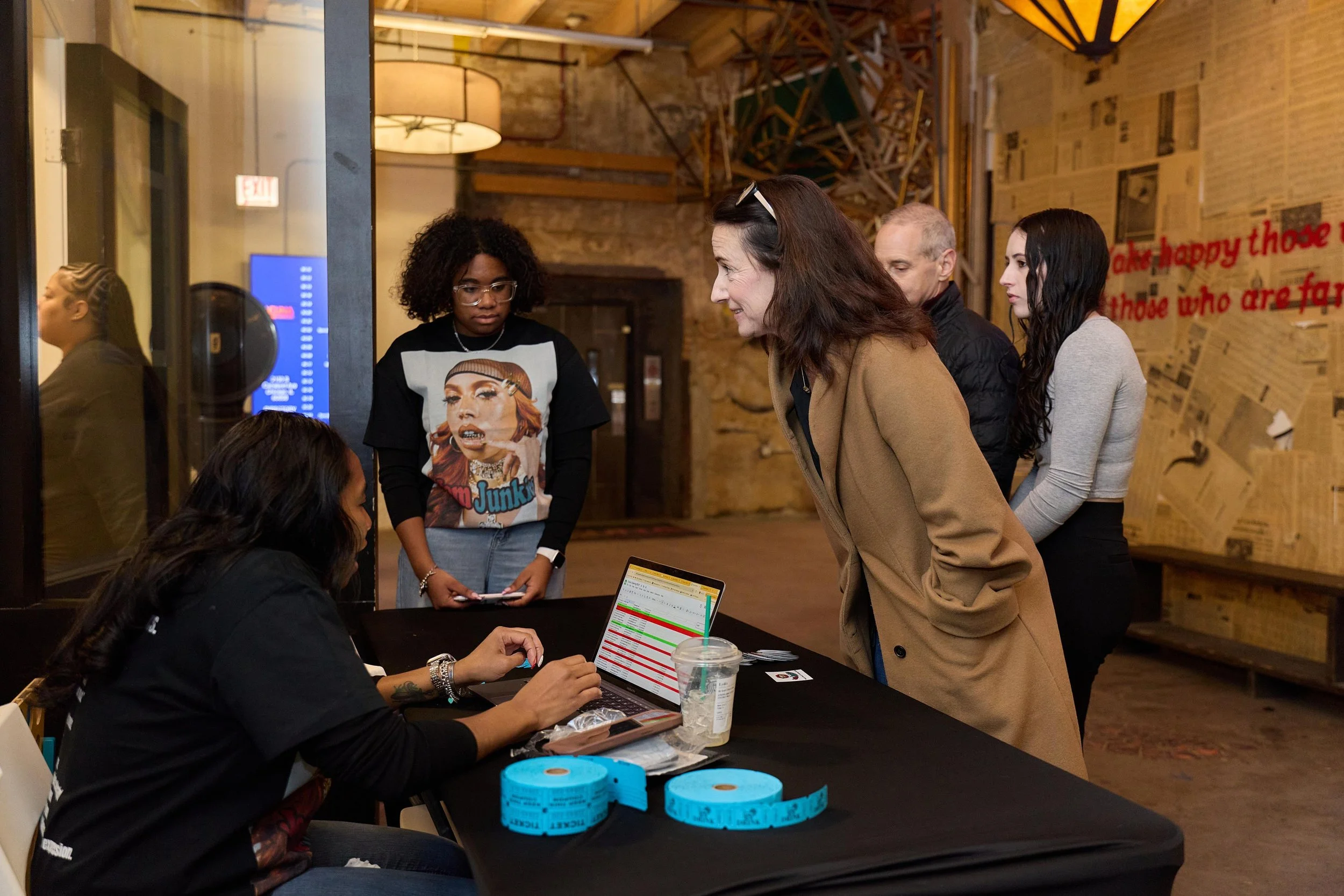 Group of five people at check-in desk in a rustic, artsy venue, with one woman sitting at computer and four standing in line at Jem Junkies Tooth Gems and  Custom Grillz in Chicago 