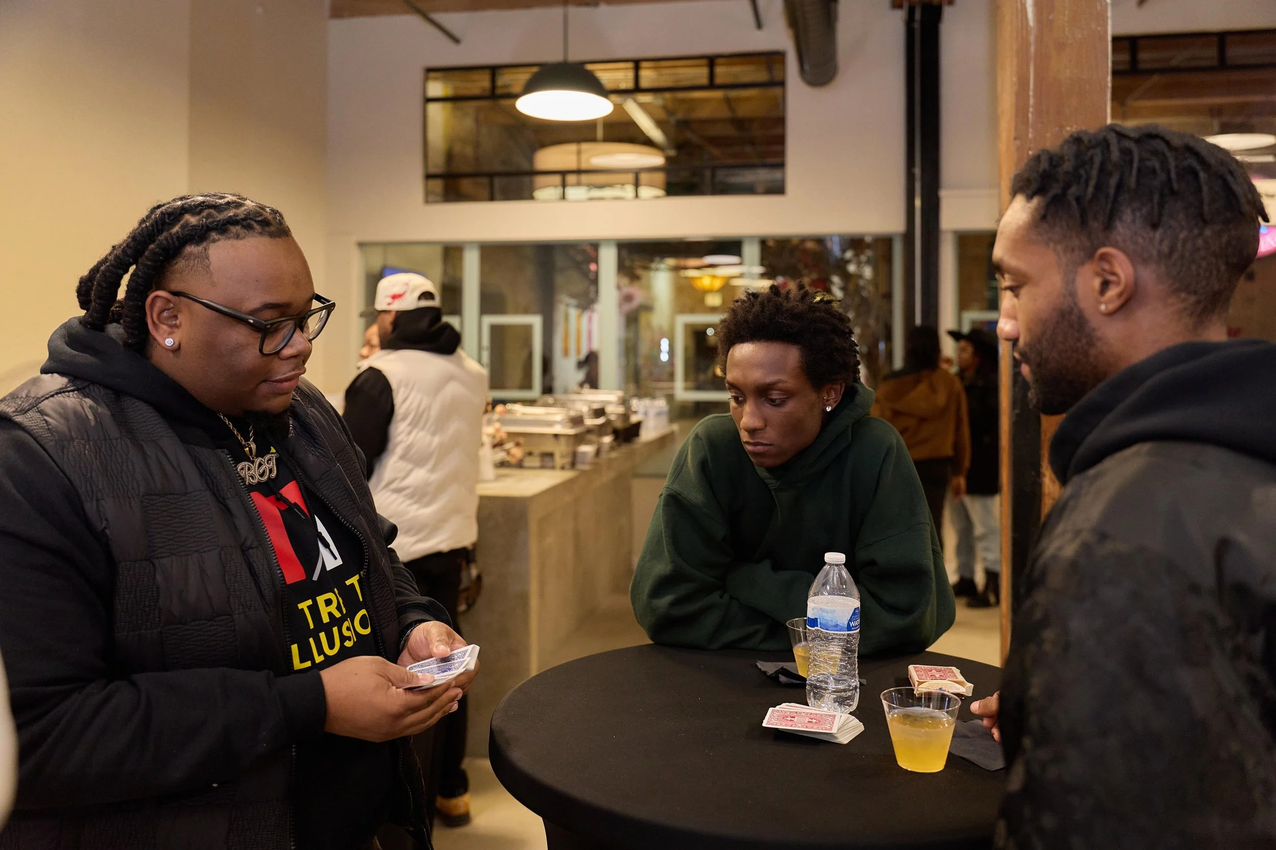 Three young people gathered around a black table playing cards at Jem Junkies Tooth Gems and  Custom Grillz in Chicago 