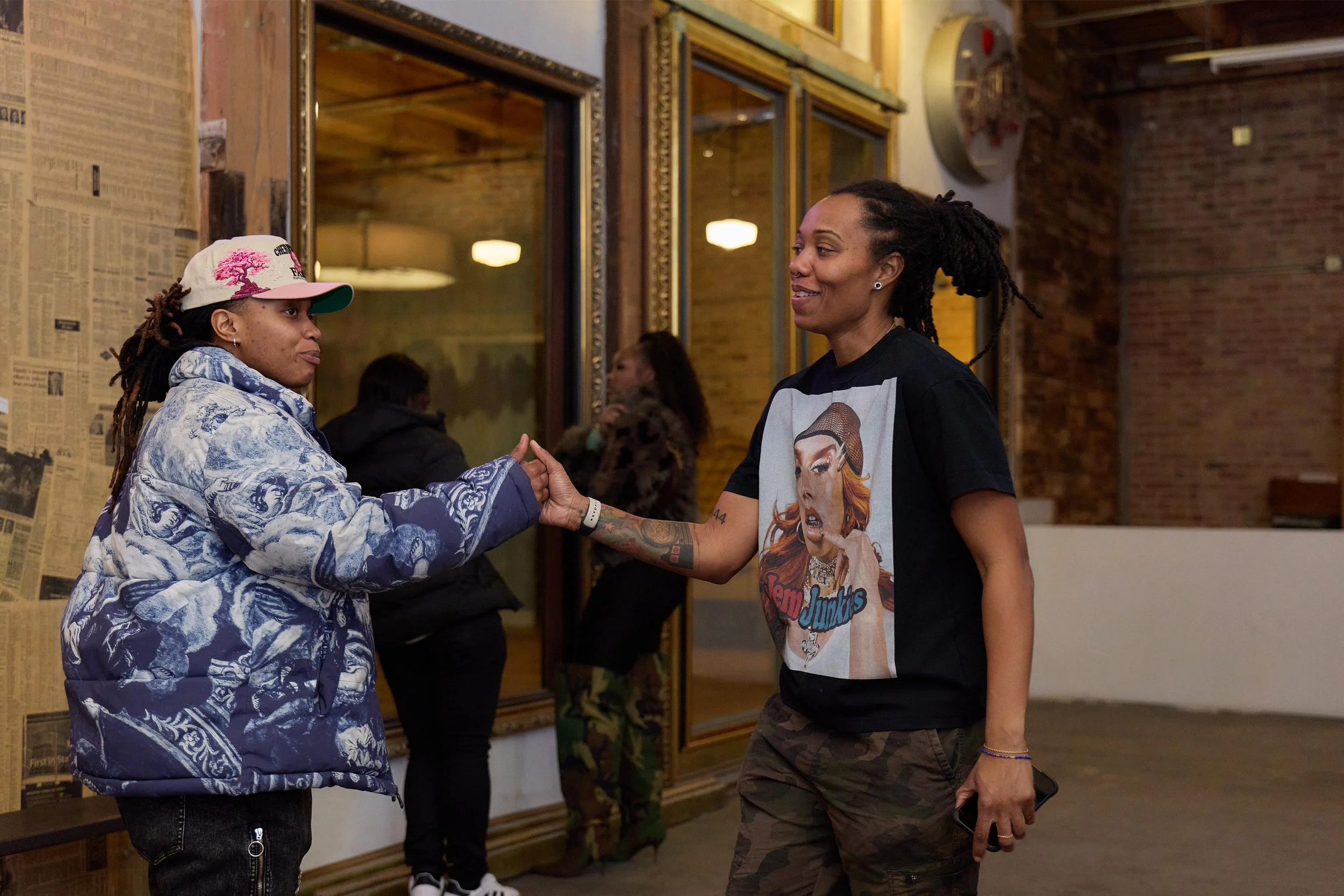 Two women shaking hands in an indoor setting, with brick walls and a window in the background at Jem Junkies Tooth Gems and  Custom Grillz in Chicago 