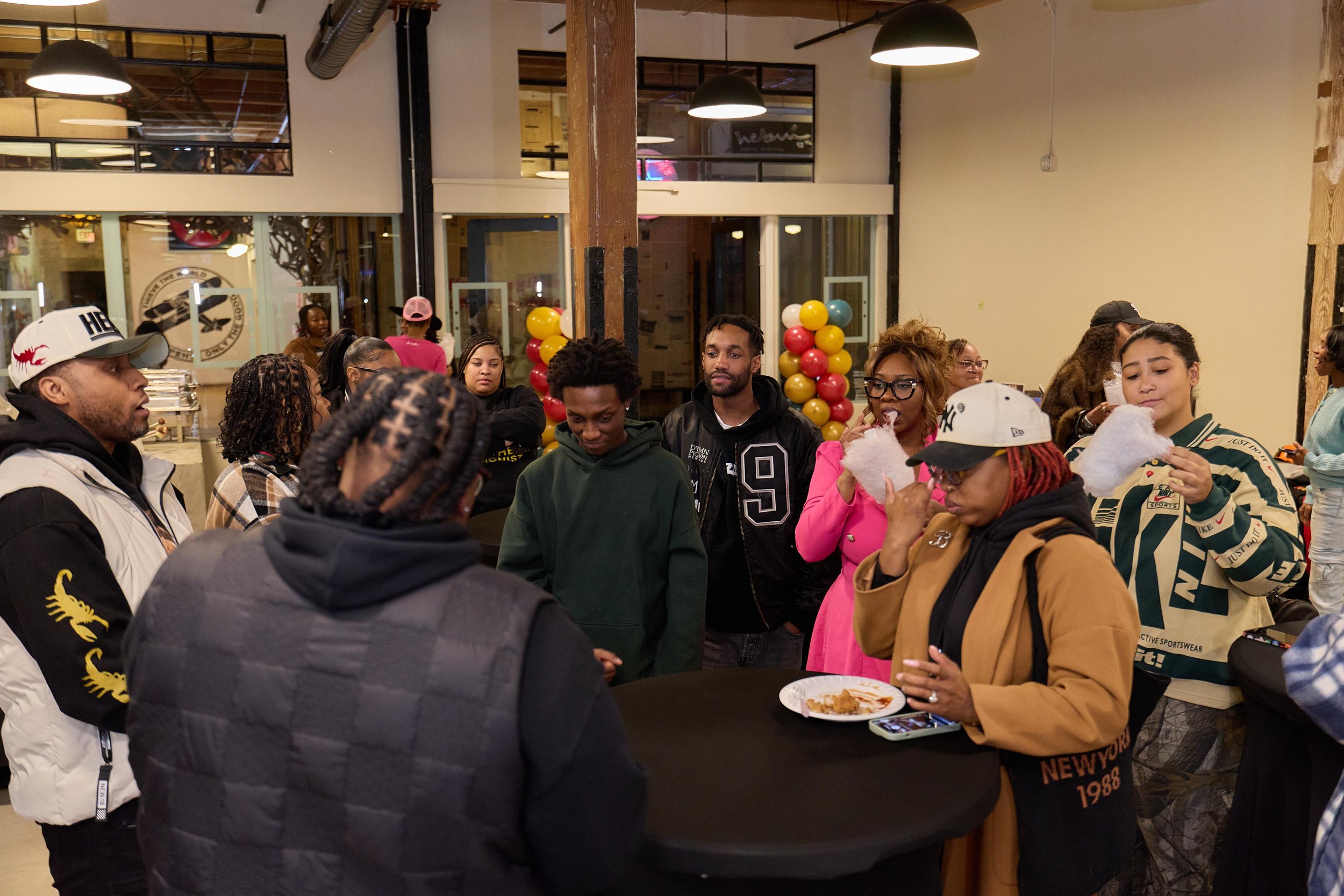 People gathered around a table at a social event or party in an indoor venue with balloons and modern decor at Jem Junkies Tooth Gems and  Custom Grillz in Chicago 