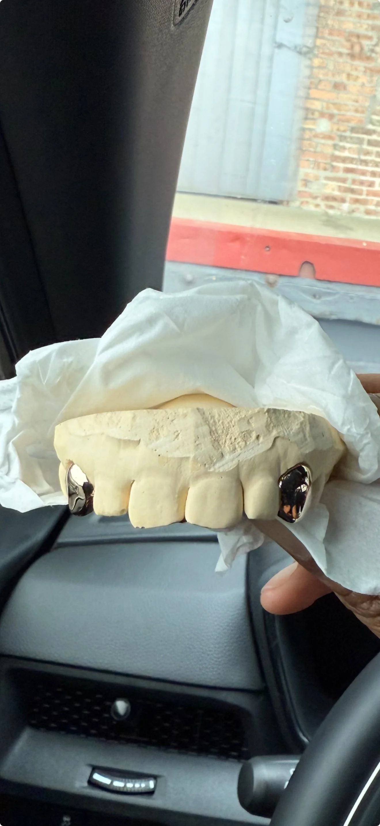 A dental mold of a person's upper teeth, with metallic dental caps on two of the front teeth, held in a hand wrapped in tissue inside a vehicle on the south side of Chicago.