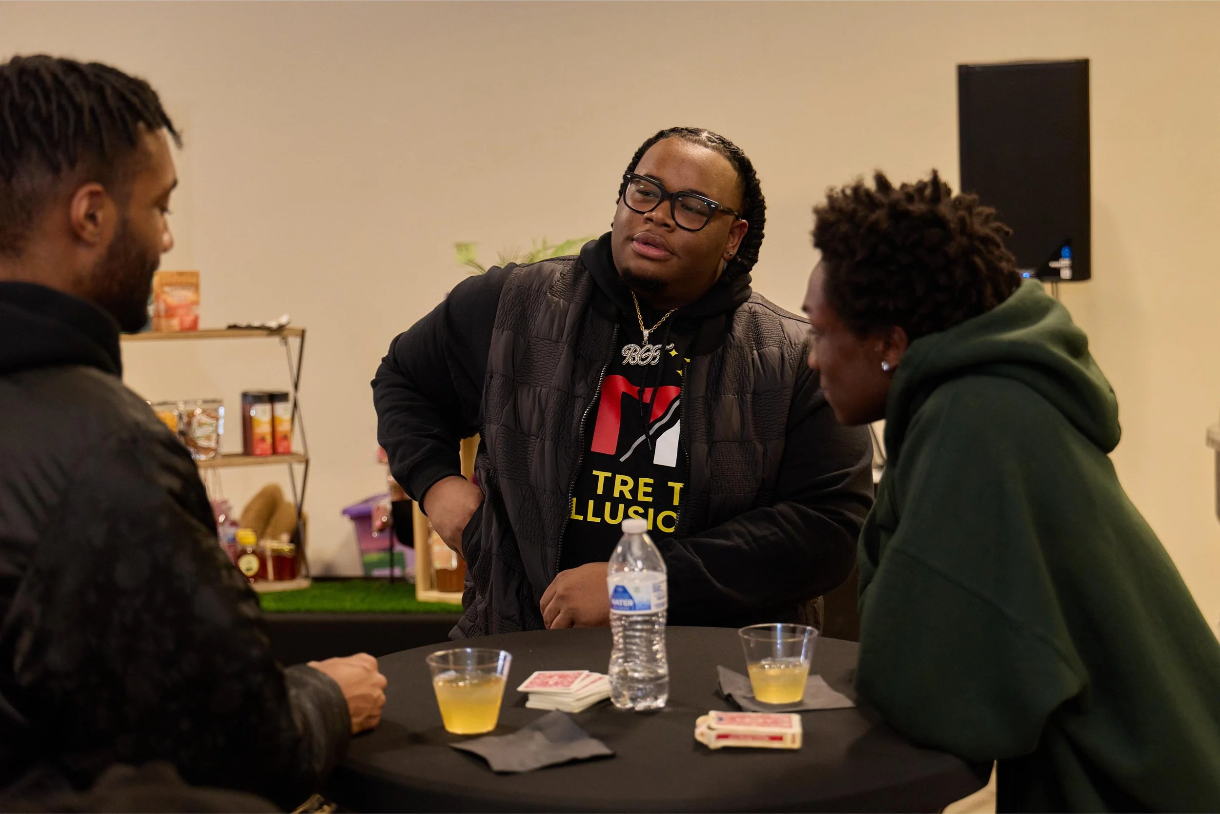 Three men gathered around a table playing cards, with two drinks and a water bottle visible at Jem Junkies Tooth Gems and  Custom Grillz in Chicago 