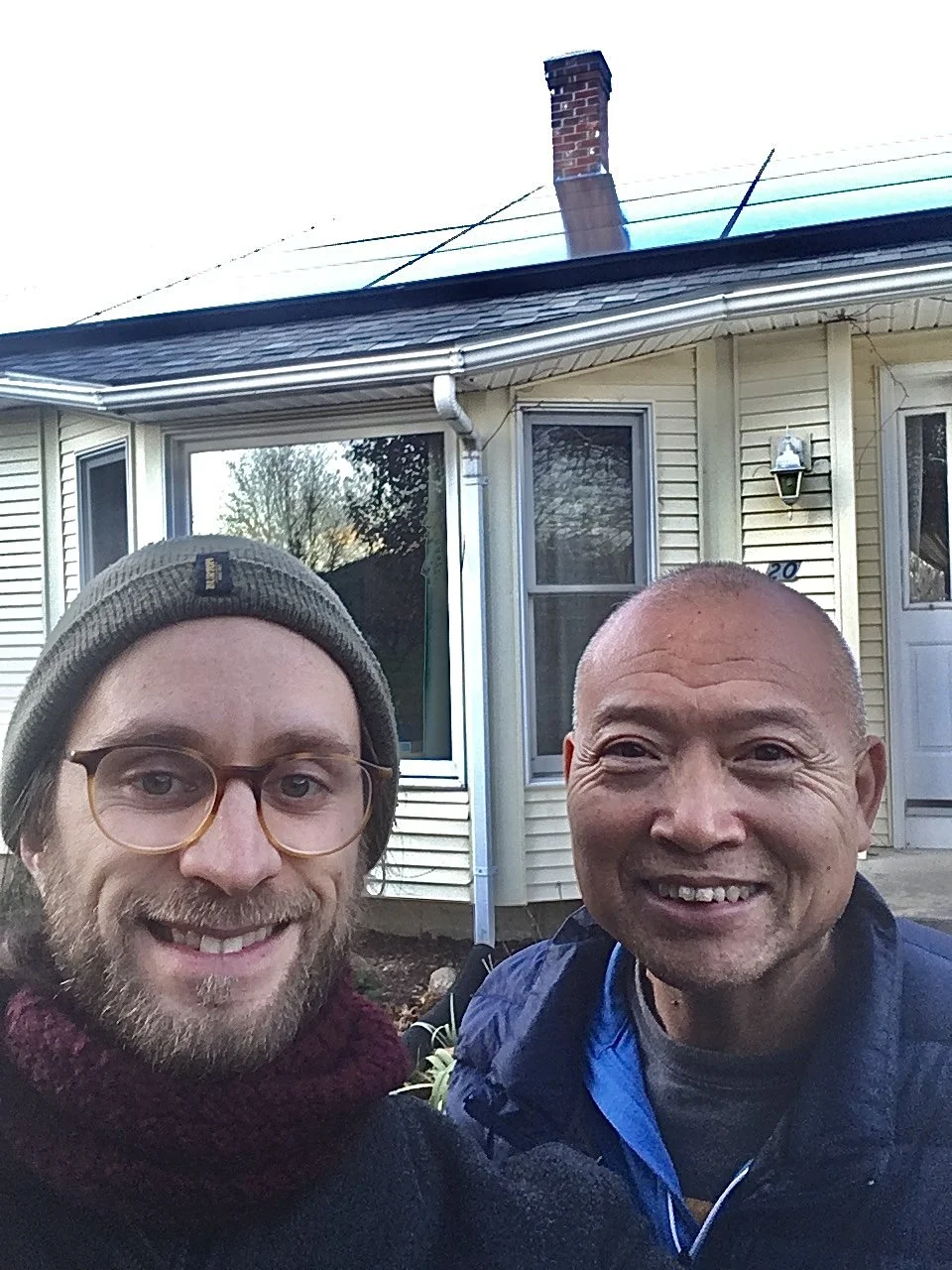 Two men smiling outdoors in front of a house.