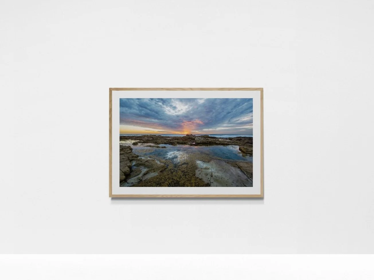 Photograph of a coastal landscape with rocks, water, and seaweed, taken during sunset with a colorful sky and clouds.