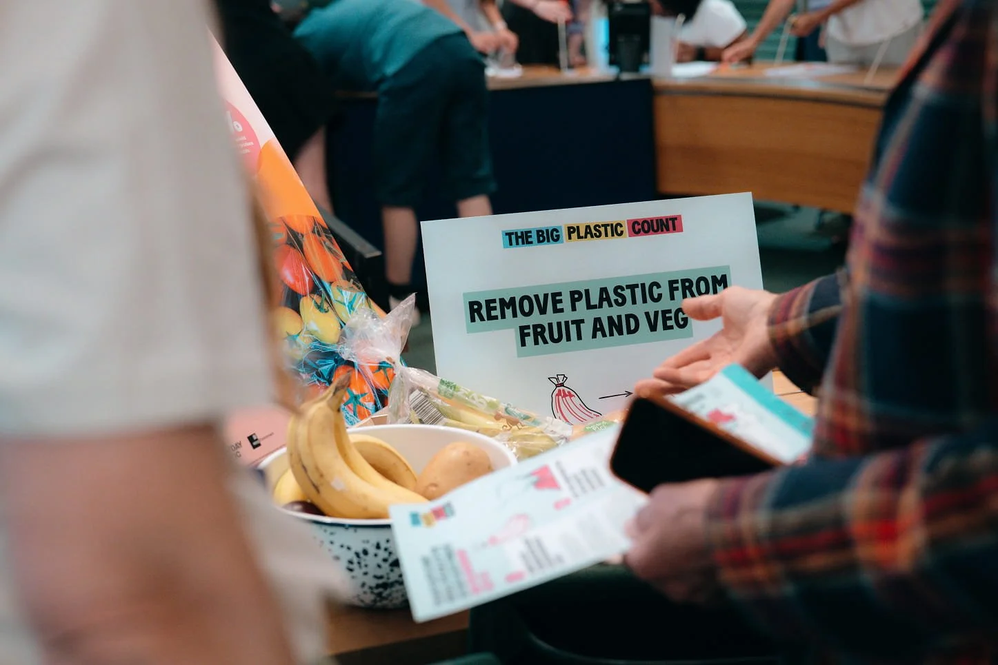 Hands pointing to a sign saying 'remove plastic from fruit and veg'