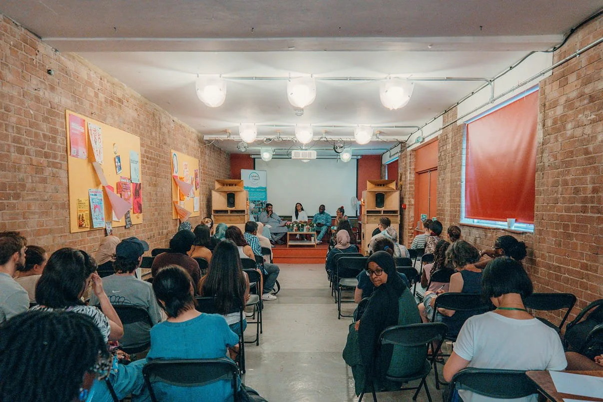 A wide shot of a panel in a colourful room speaking to a seated audience