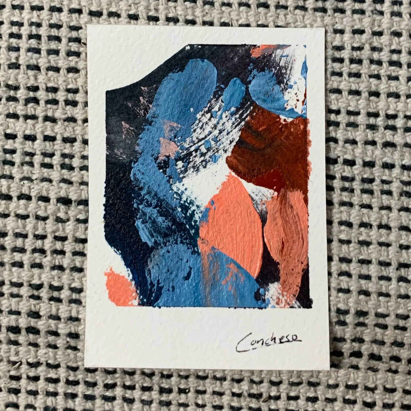 Una tarjeta con una pintura abstracta en tonos azules, negros y naranjas, con la firma 'Concheo' en la parte inferior derecha.