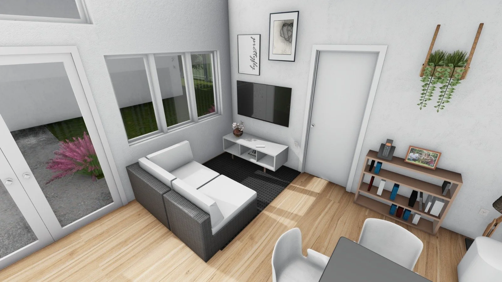 Living room with gray and white sectional sofa, black rug, wall-mounted TV, picture frames, a bookshelf with books and photo, white door, and a wall-mounted plant