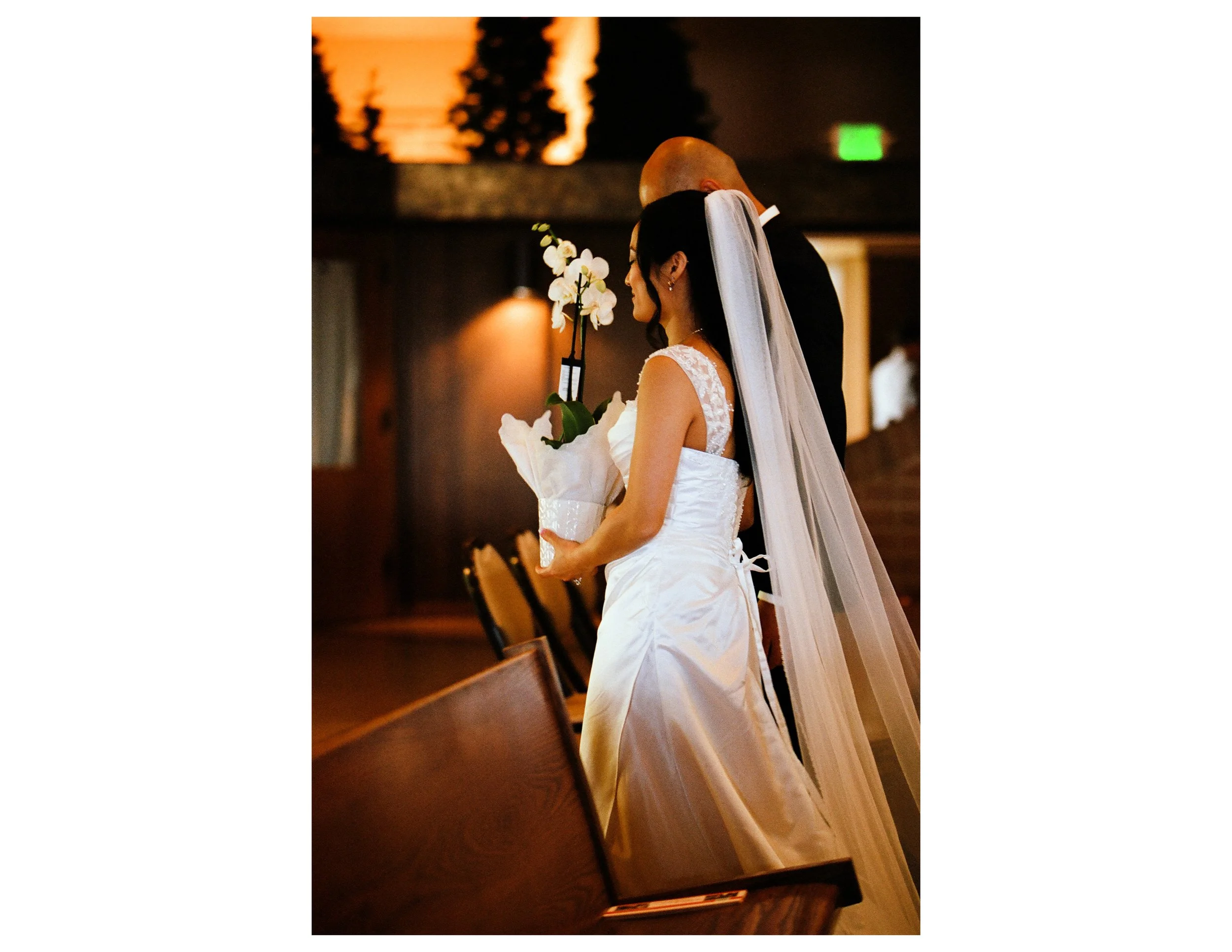 A bride and groom share a quiet moment during their wedding ceremony, with the bride holding a bouquet of white orchids.