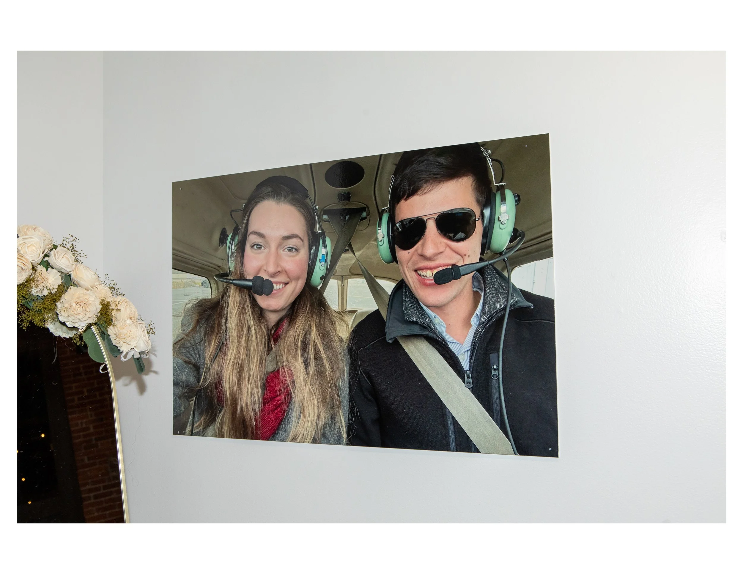 Two people in an aircraft, wearing headsets and sunglasses, smiling for a selfie.