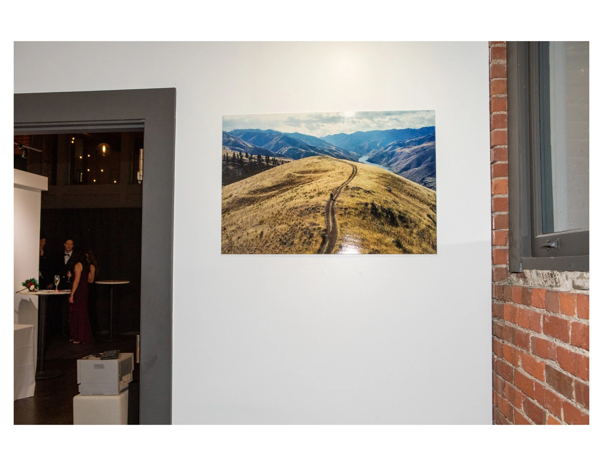 Interior of an art gallery displaying landscape photography, with a mountain scene on the wall and part of a brick wall visible.
