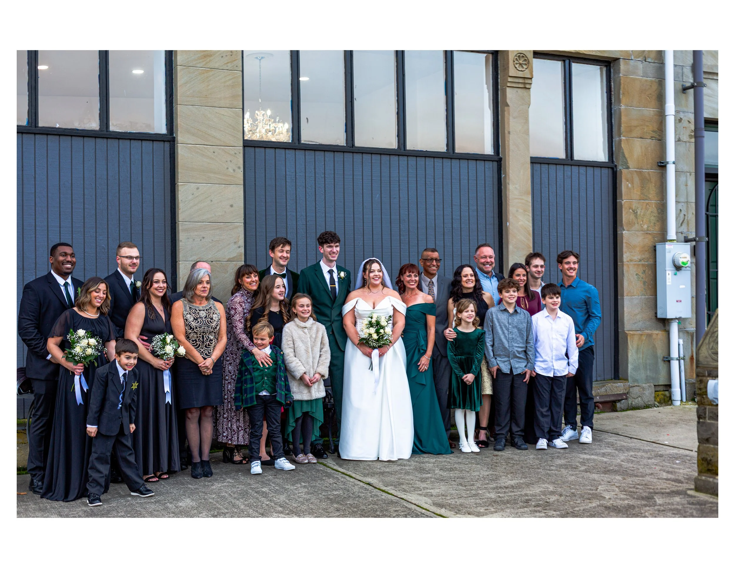 Group of diverse people at a wedding outside a building, smiling and dressed in formal and semi-formal attire.