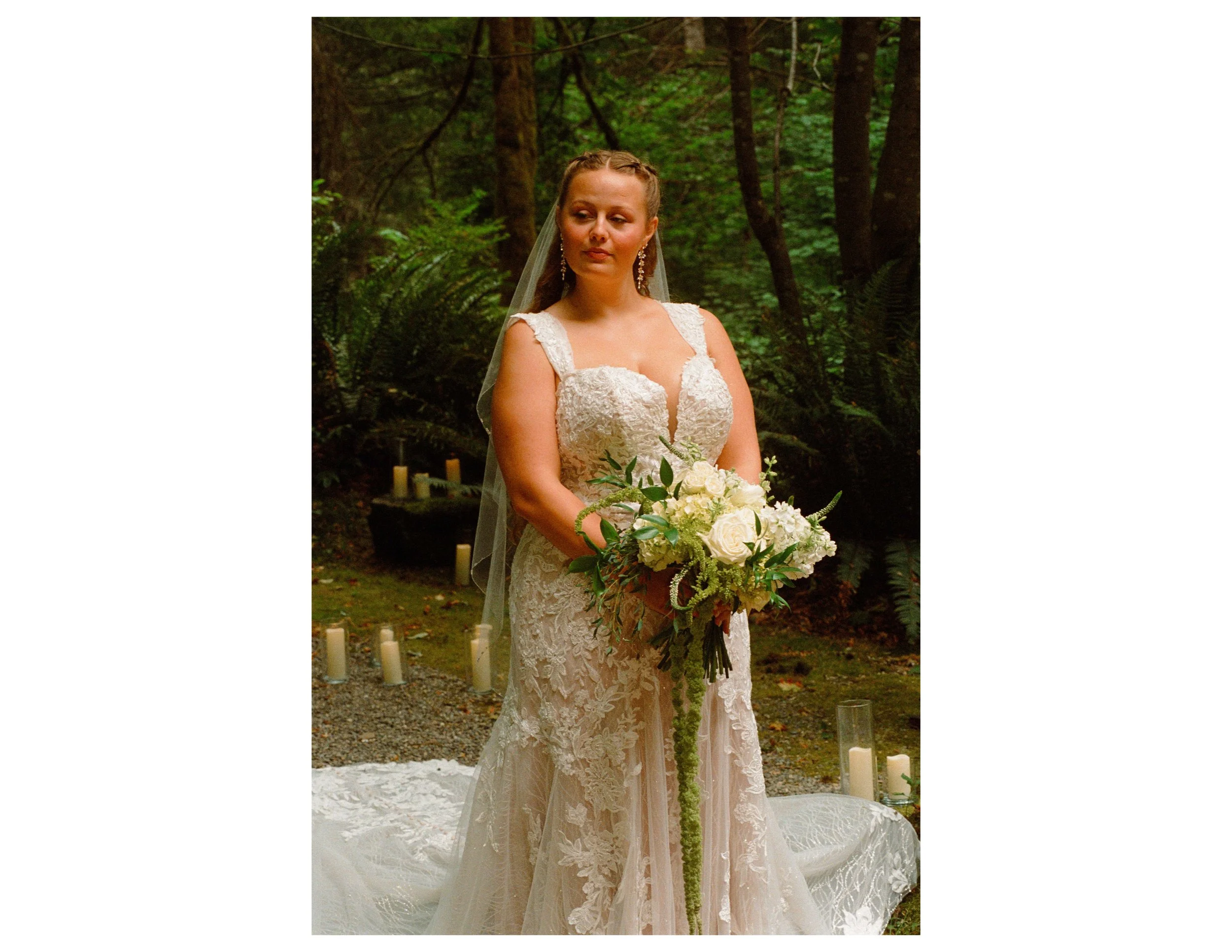 A bride in a lace wedding dress holding a bouquet of white flowers in a forest setting during her wedding ceremony.