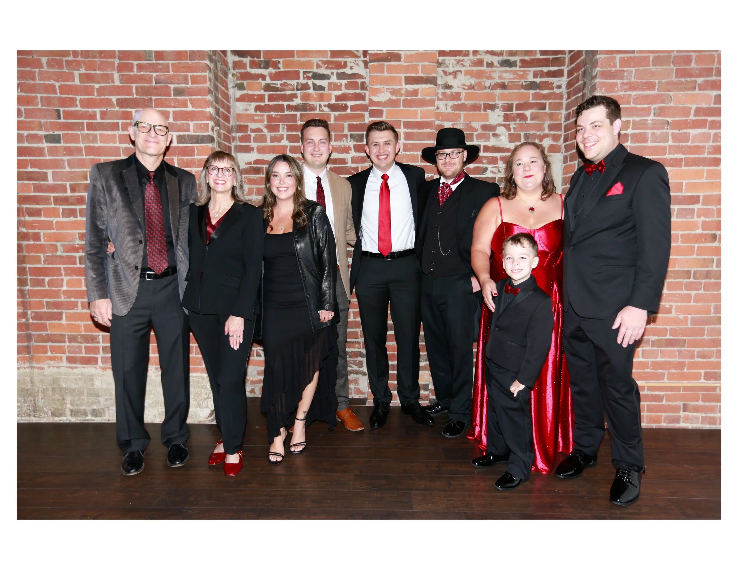 Group of people dressed in formal and semi-formal attireposing in front of a brick wall for a photo.