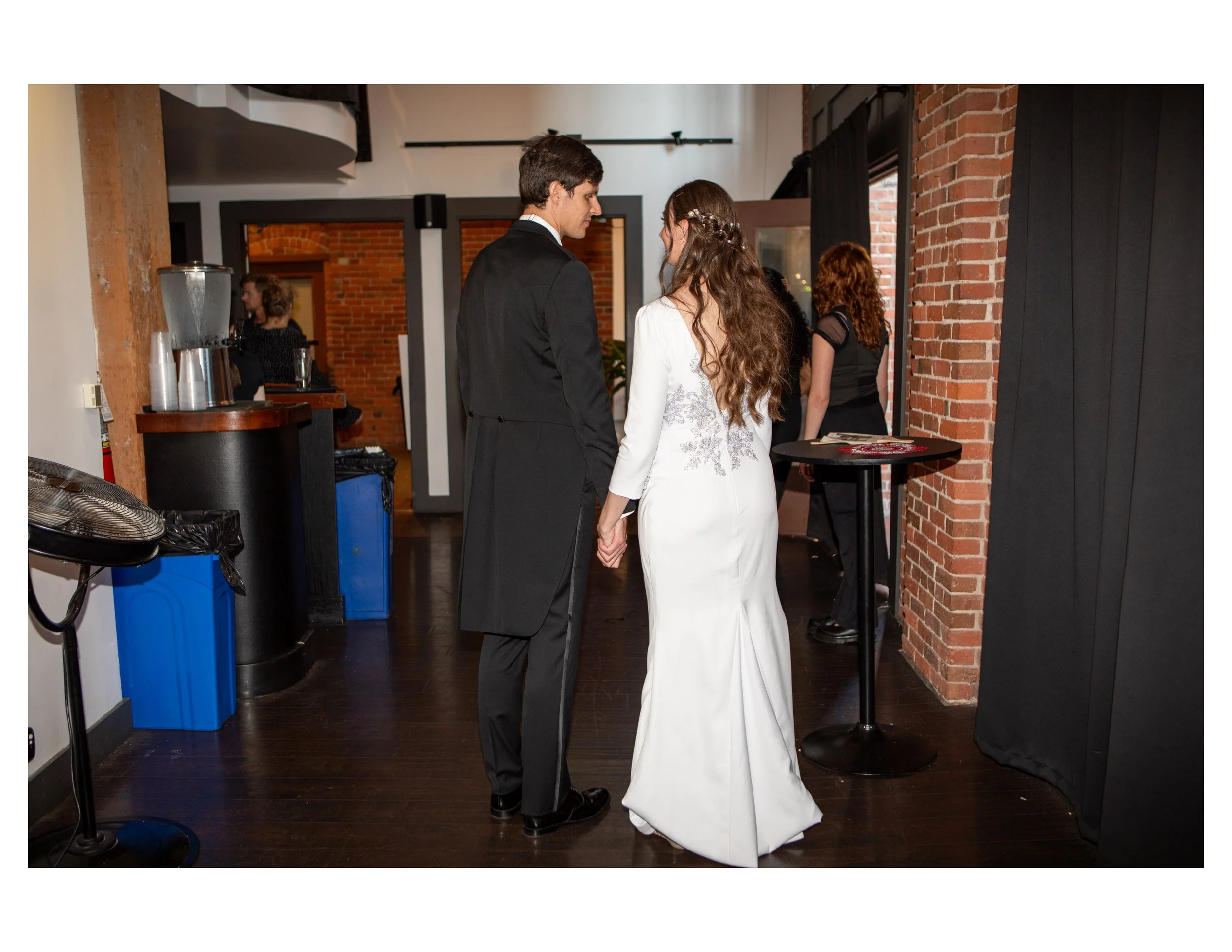 A bride and groom holding hands during their wedding ceremony in an indoor venue with brick walls and dark flooring.