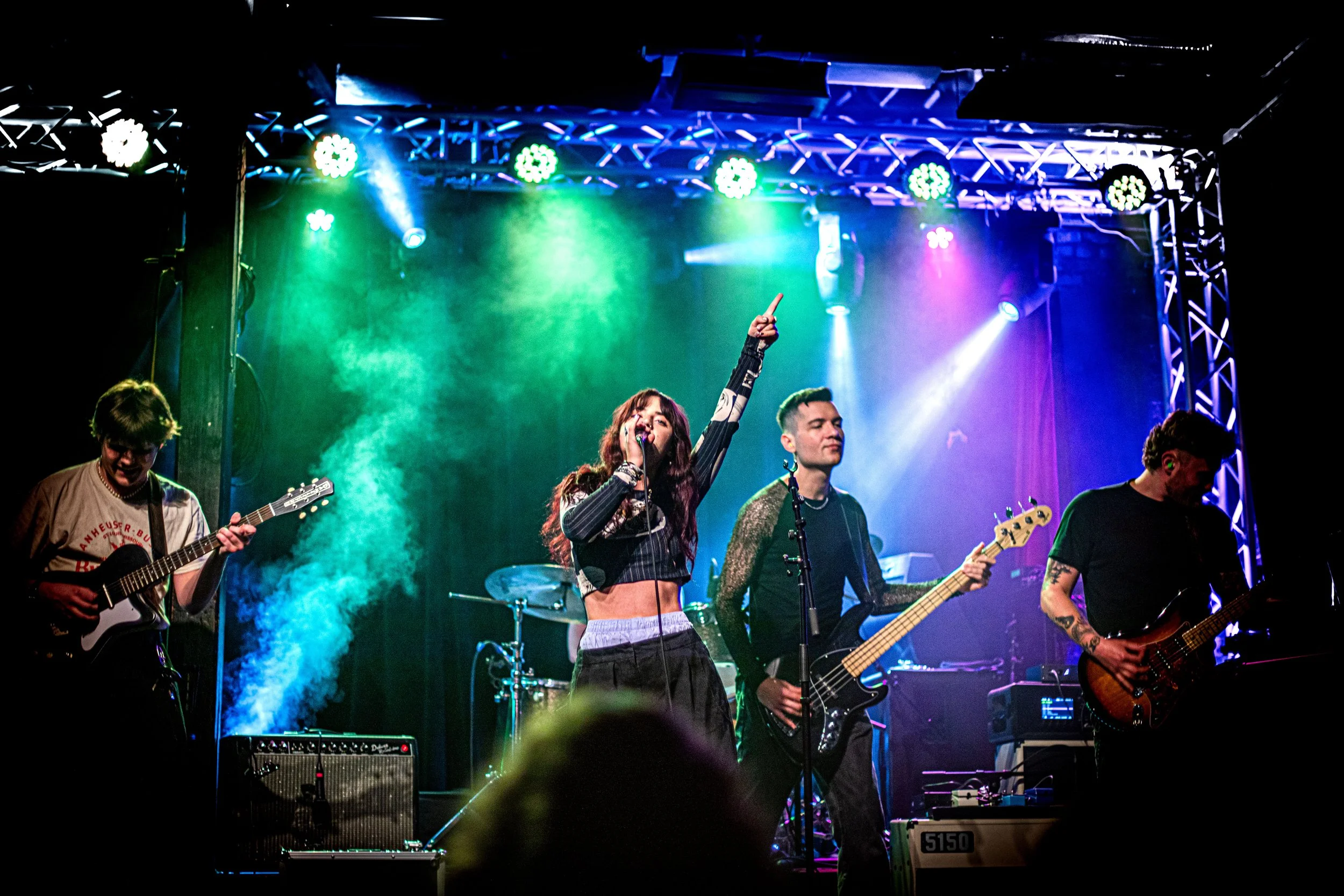 A band performs on stage with colorful lighting, featuring a female lead singer and three male guitarists