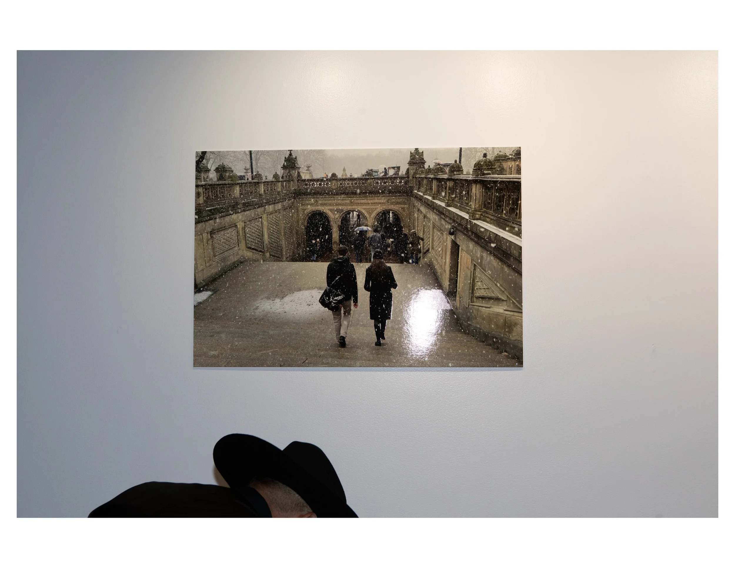 View from a white structure looking onto a rainy, historic European city bridge with people carrying umbrellas.