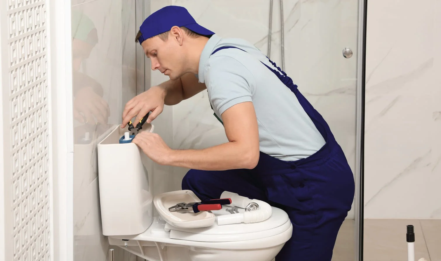 Plumber fixing toilet cistern with tools in bathroom.