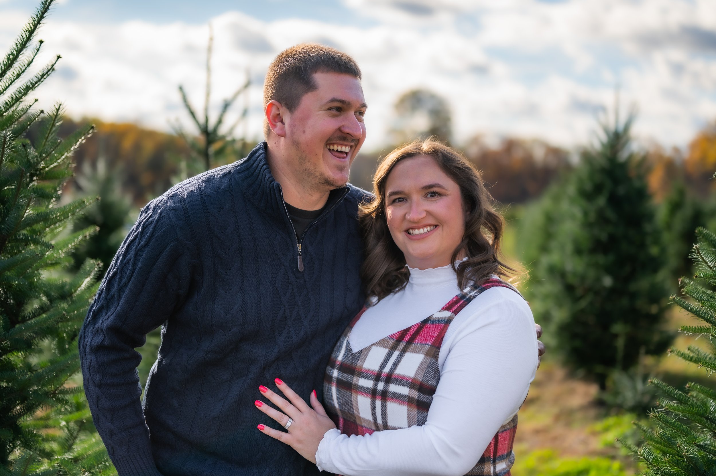A happy couple poses for the camera, husband is laughing and wife is happily smiling at the camera