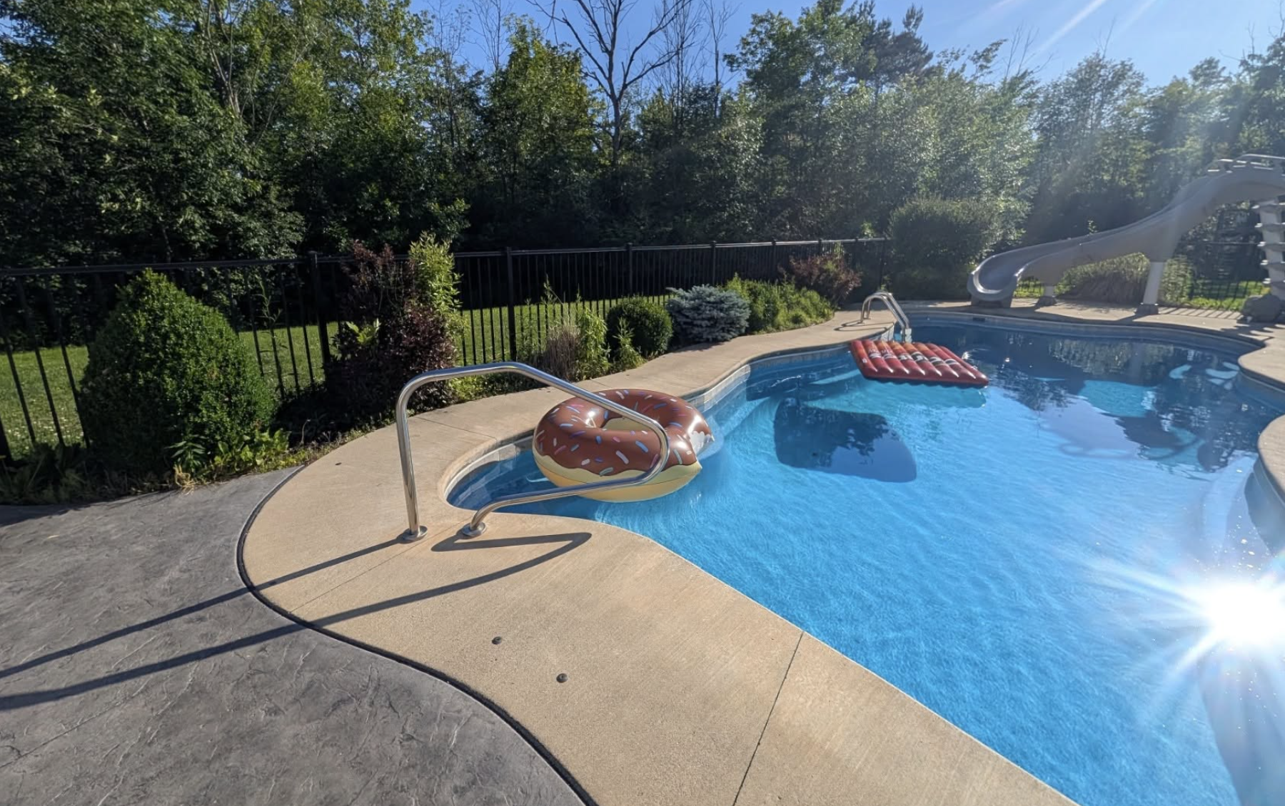 Backyard landscape cleanup featuring maintained pool landscaping, fresh mulch, trimmed plants, and healthy lawn.
