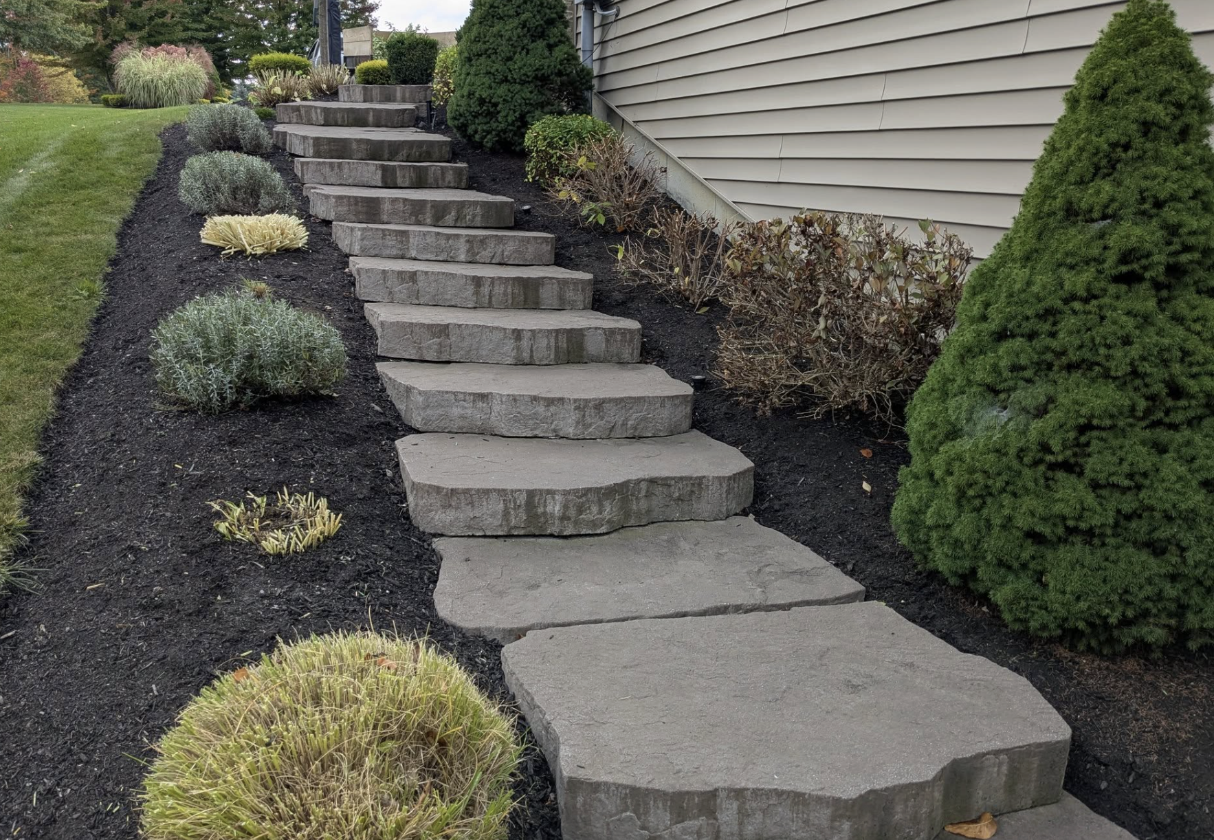 Concrete stepping stones leading up a landscaped garden slope with bushes and plants on the sides.