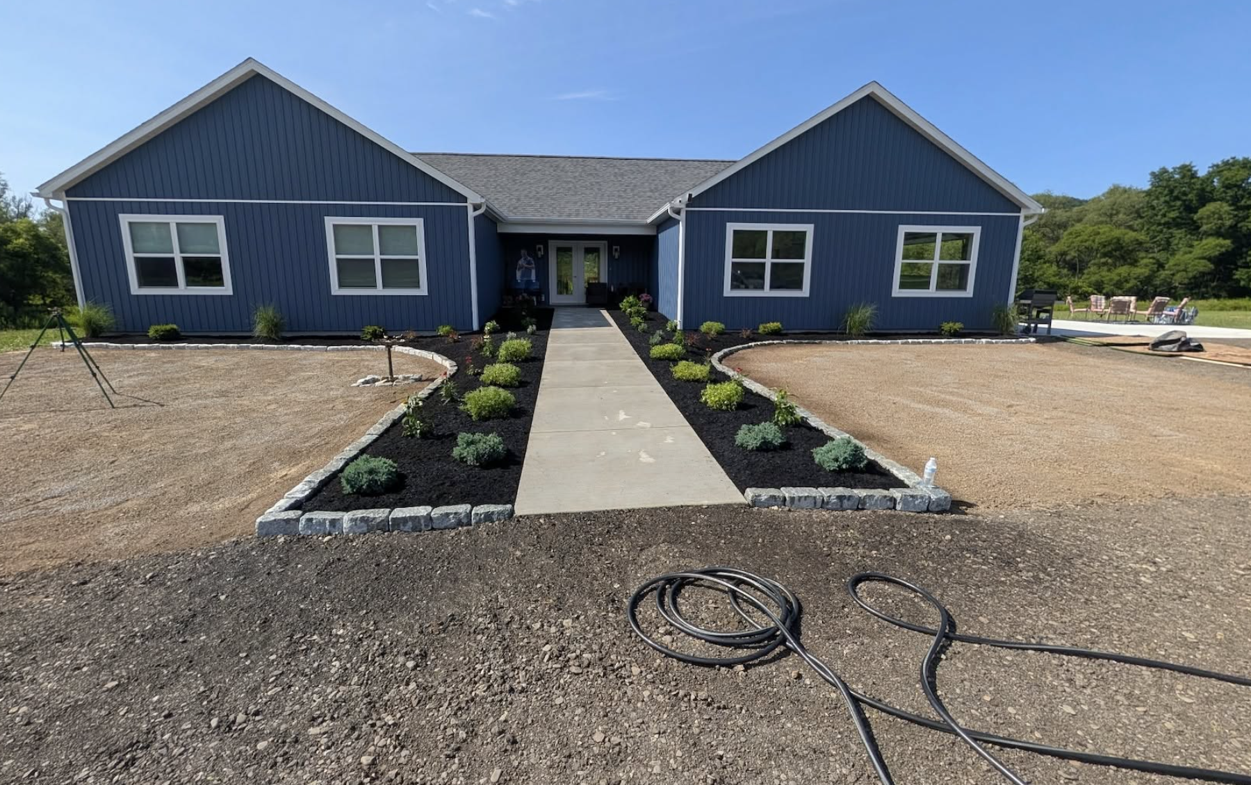 Completed landscape installation featuring fresh plantings, yard seeding, mulch beds, and granite cobblestone edging by Kielty Landscaping.