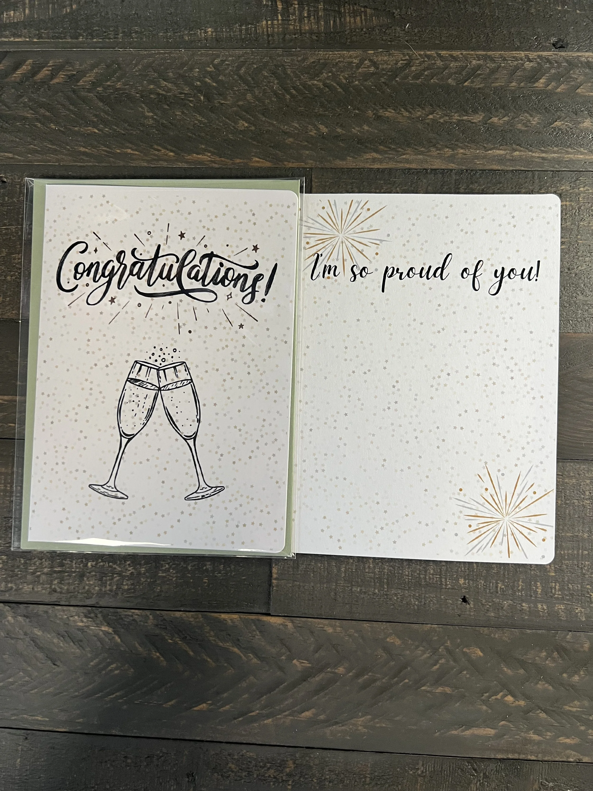 Open congratulations card showing inside message “I’m so proud of you!” with champagne glass design on front