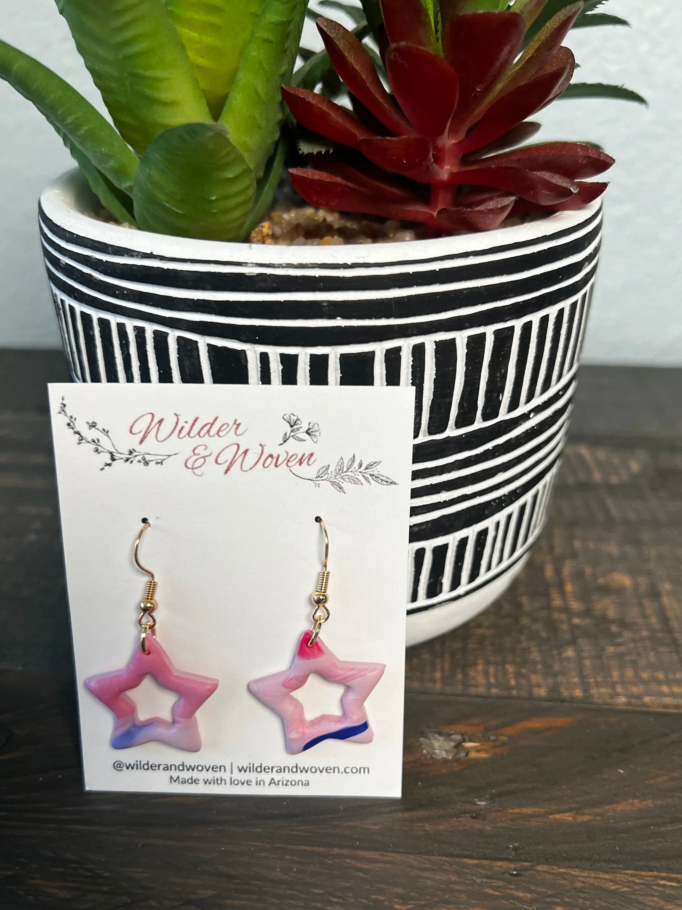 Handmade blush pink marbled polymer clay open star earrings with red, white, and blue accents hanging from gold fishhook ear wires.