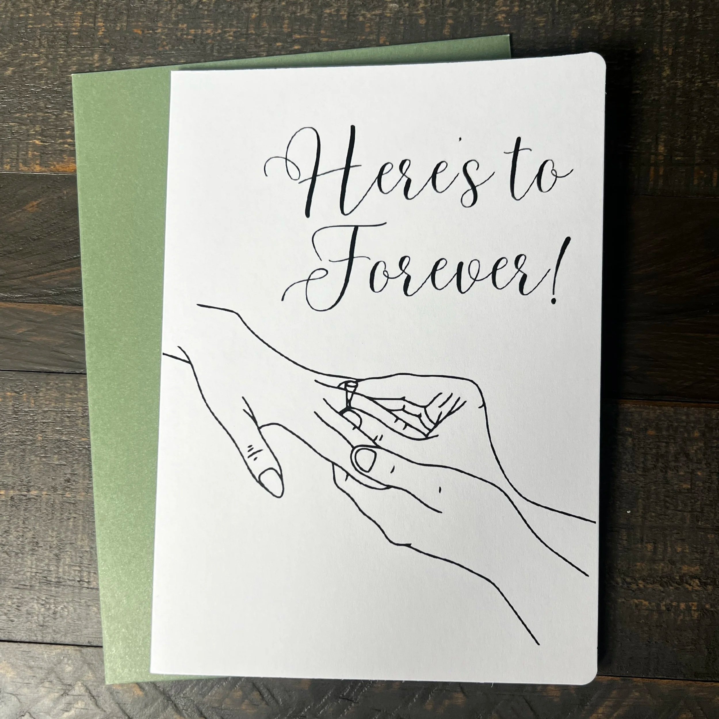 Front of Here's to Forever engagement card with coordinating sage green envelope.