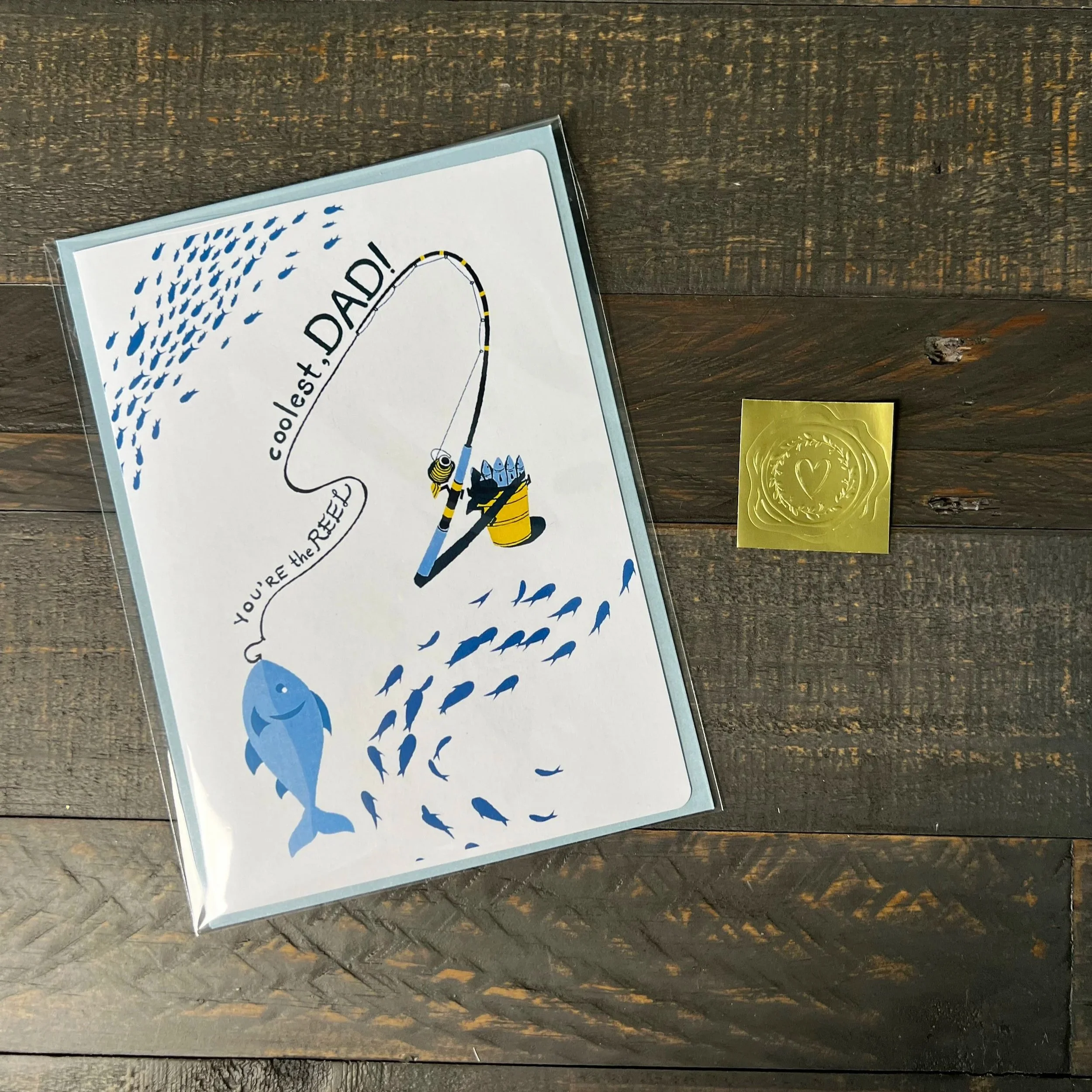 Fishing Father’s Day card styled with blue envelope and gold wax seal sticker on wood surface