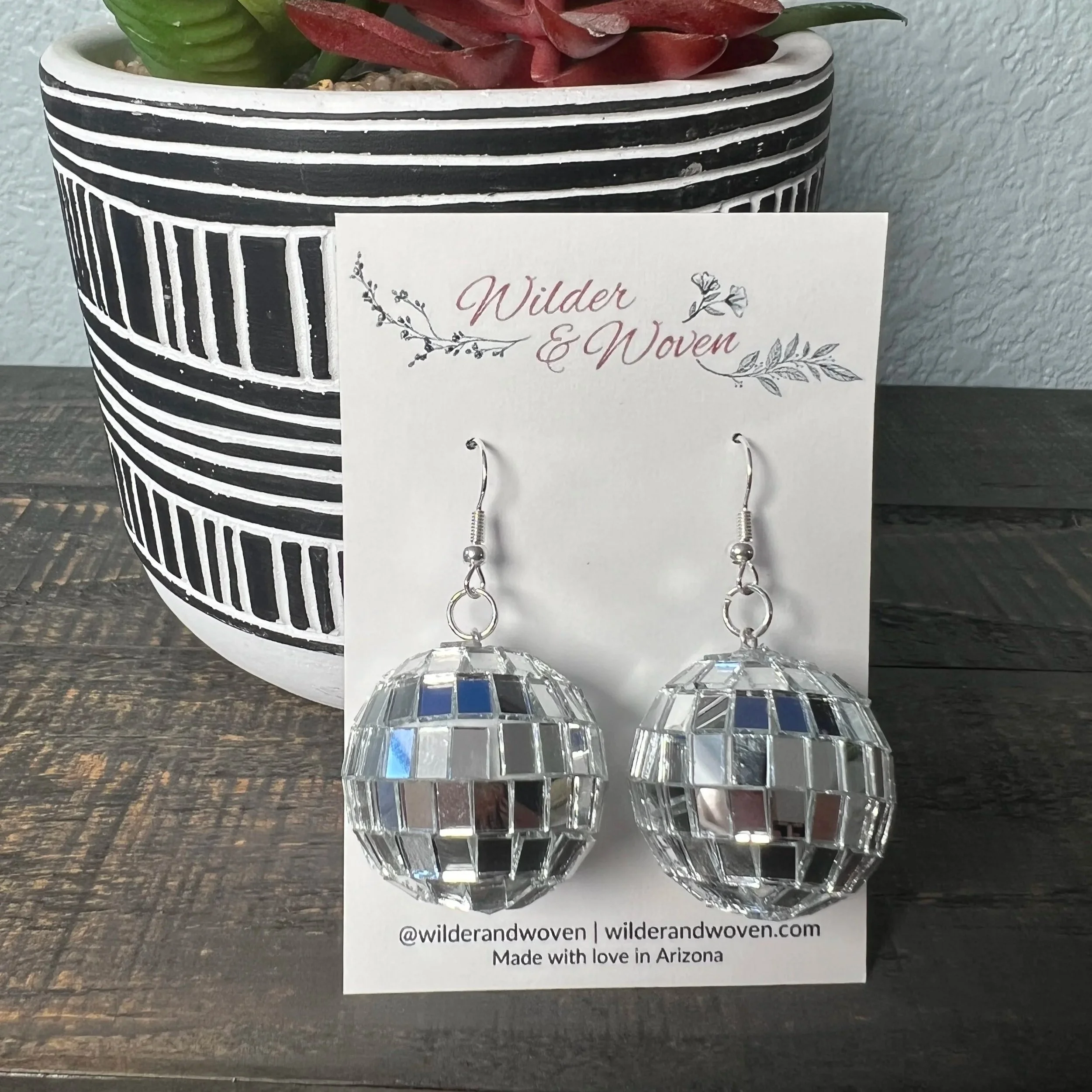 Silver mirrored disco ball charm earrings displayed on a Wilder & Woven branded jewelry card.