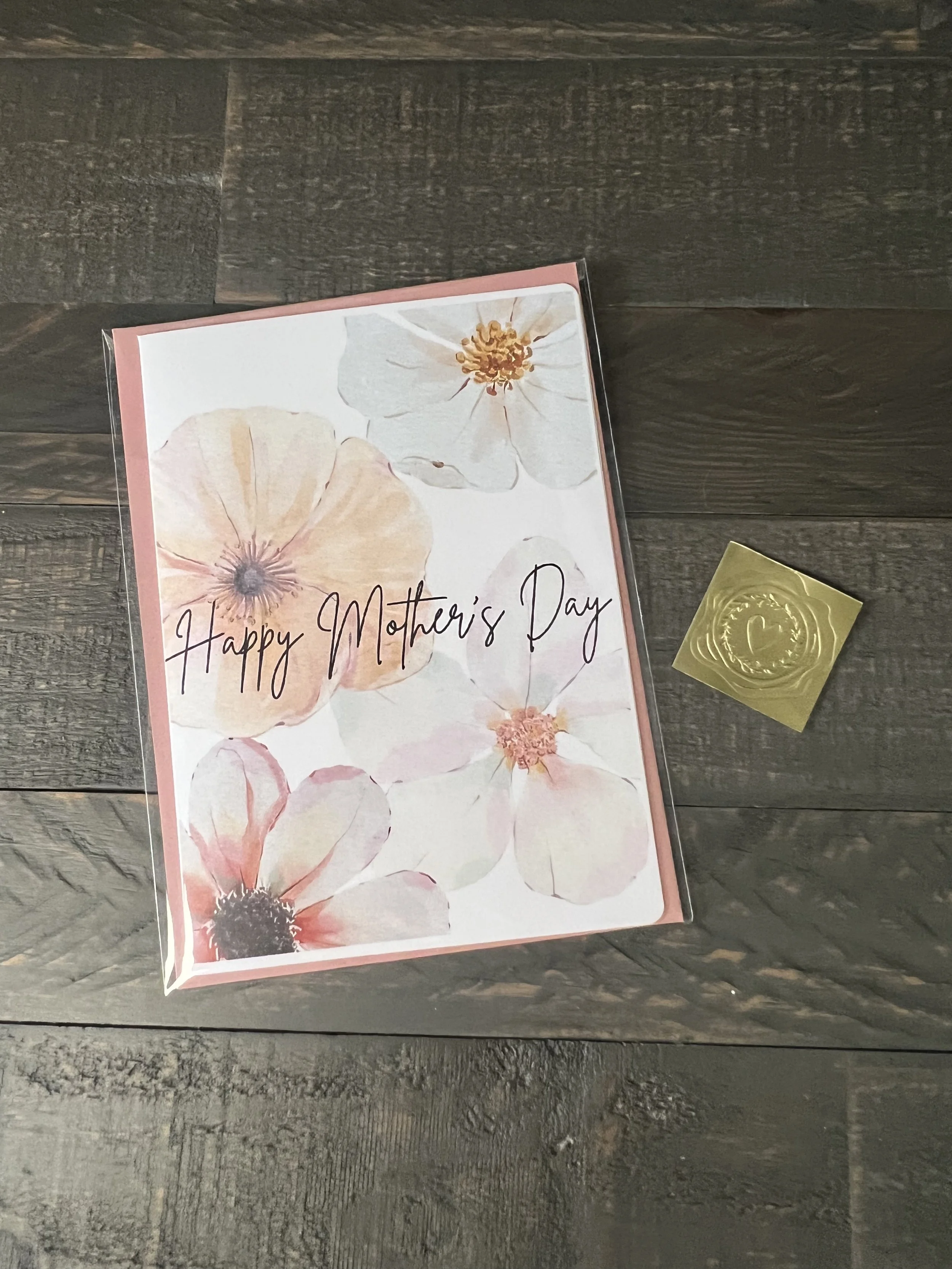 Mother’s Day card featuring soft blush and ivory watercolor flowers with “Happy Mother’s Day” script, paired with a blush envelope and gold wax seal sticker on a wooden background