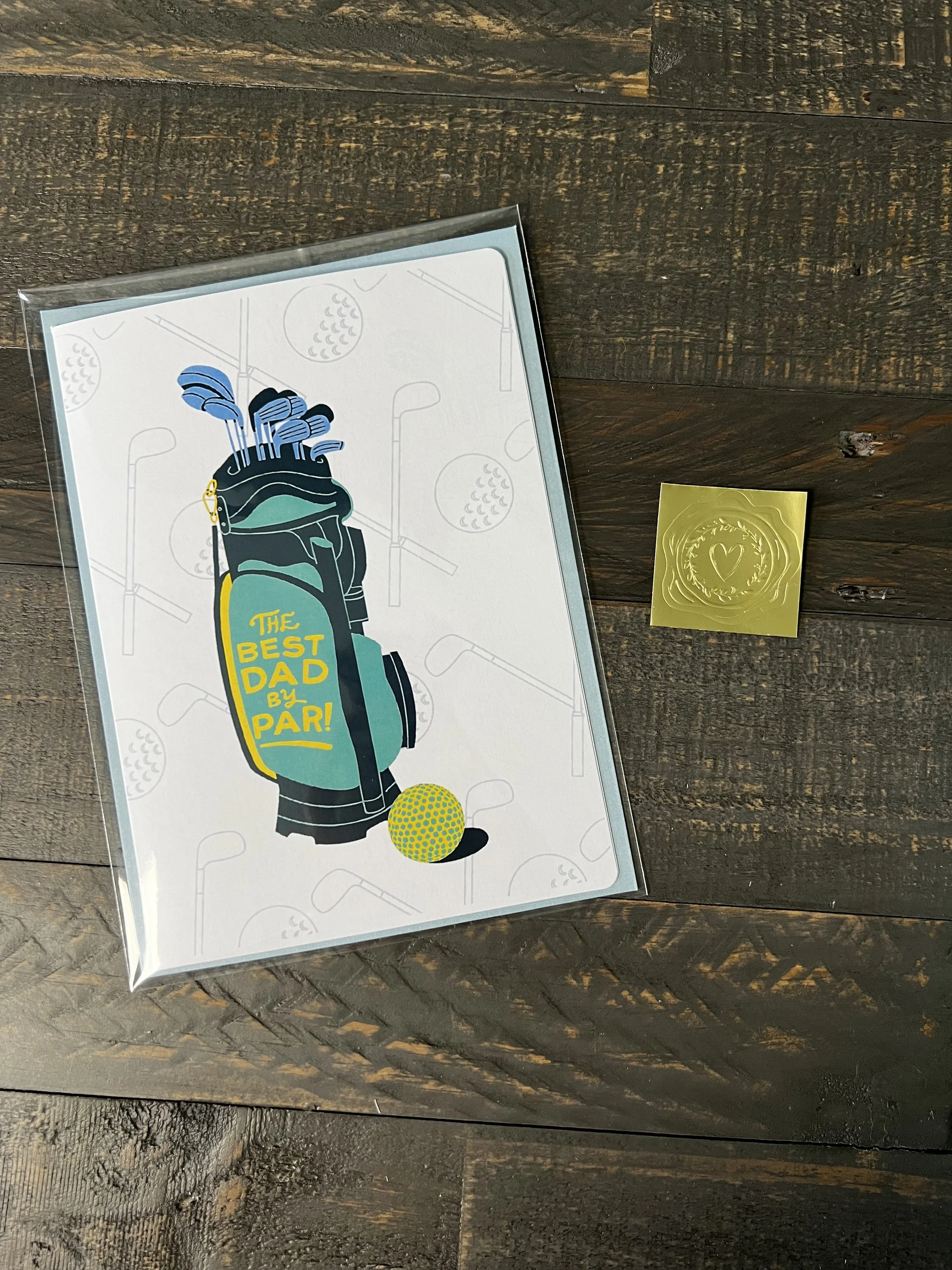 Golf Father’s Day card styled with light blue envelope and gold wax seal sticker on wood surface