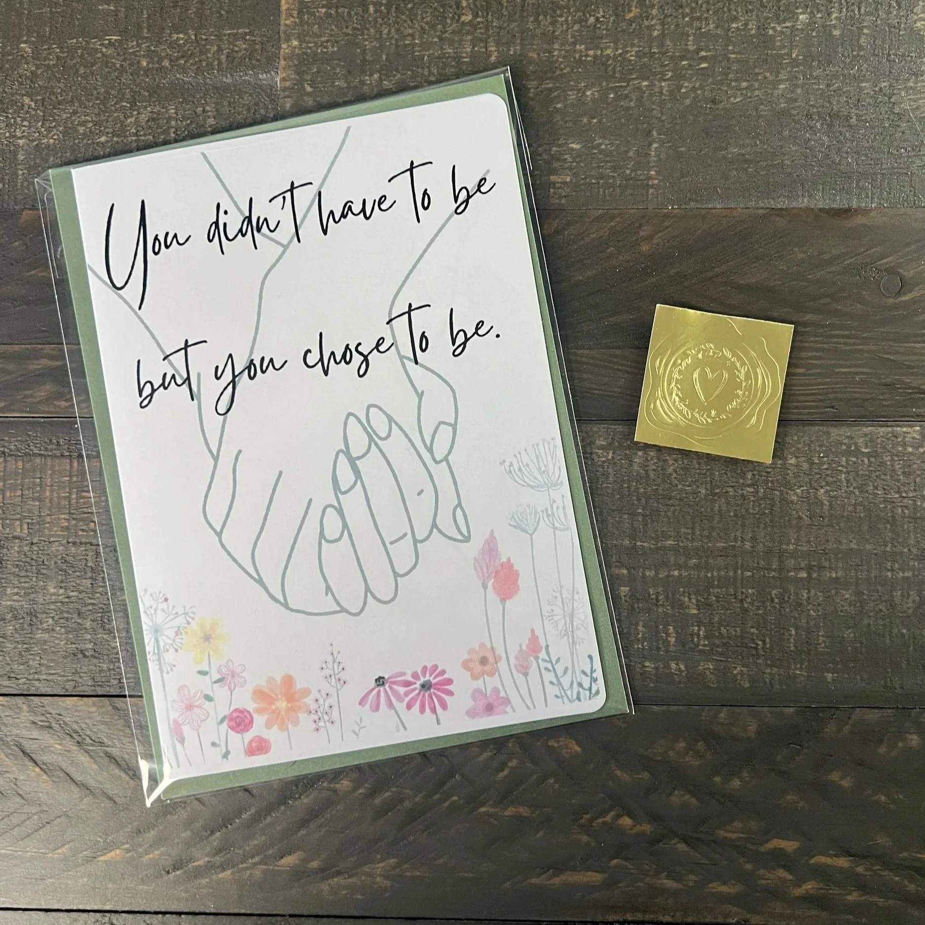 Packaged Mother’s Day card with line art hands design, sage green envelope, and gold wax seal sticker on wood surface