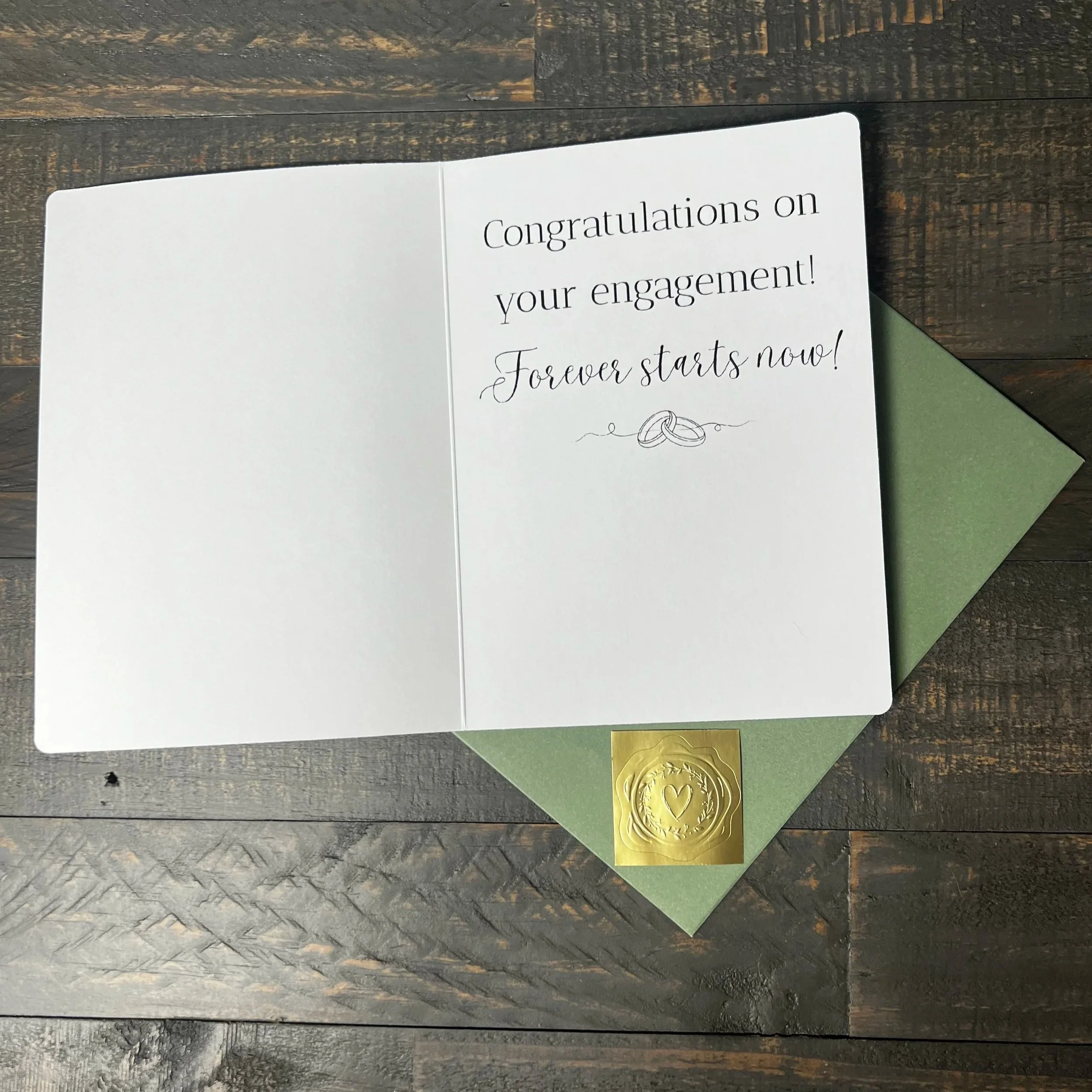 Open Here's to Forever engagement card with coordinating sage green envelope and gold wax seal style sticker.