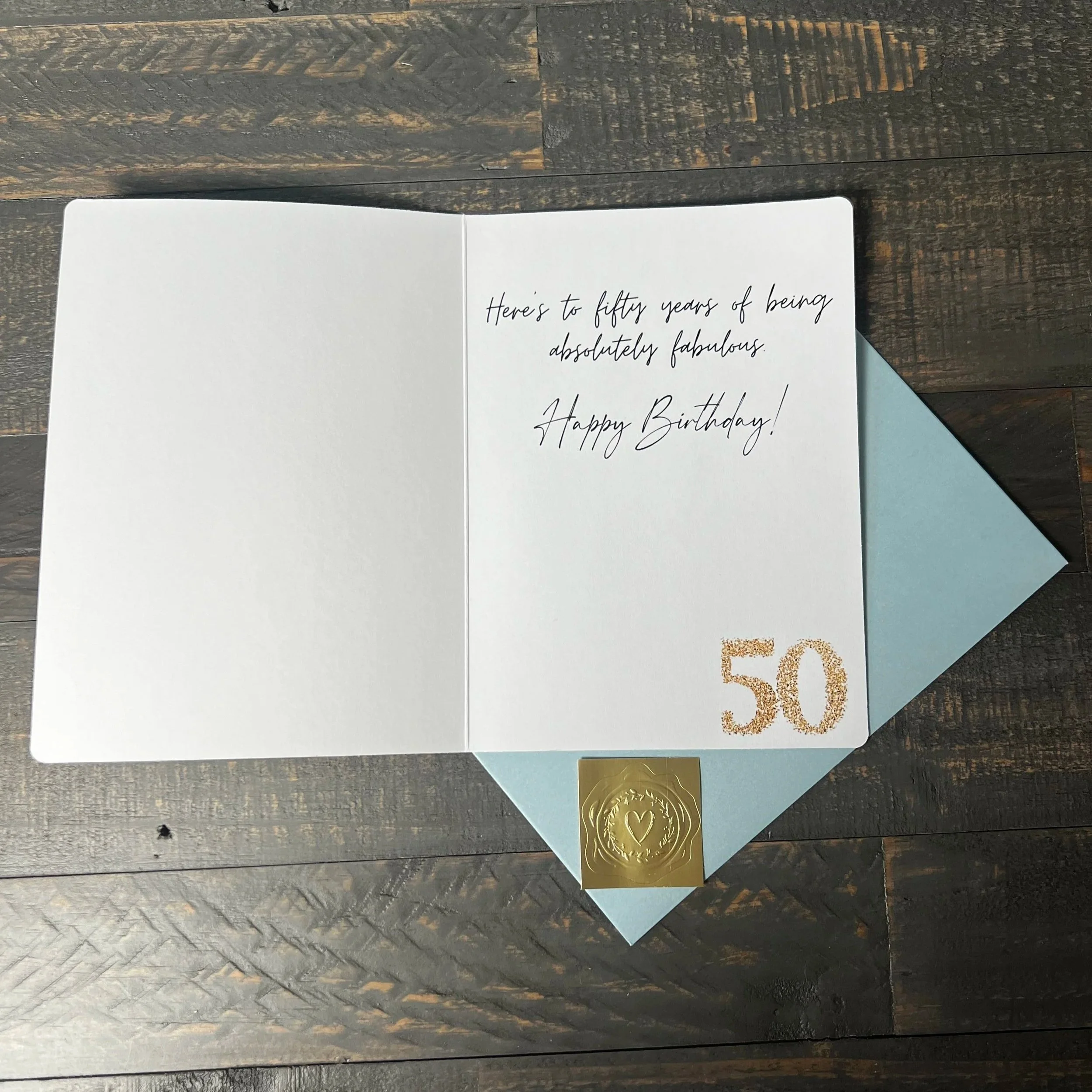 Open Fifty & Fabulous birthday card with coordinating soft blue envelope and gold wax seal style sticker.