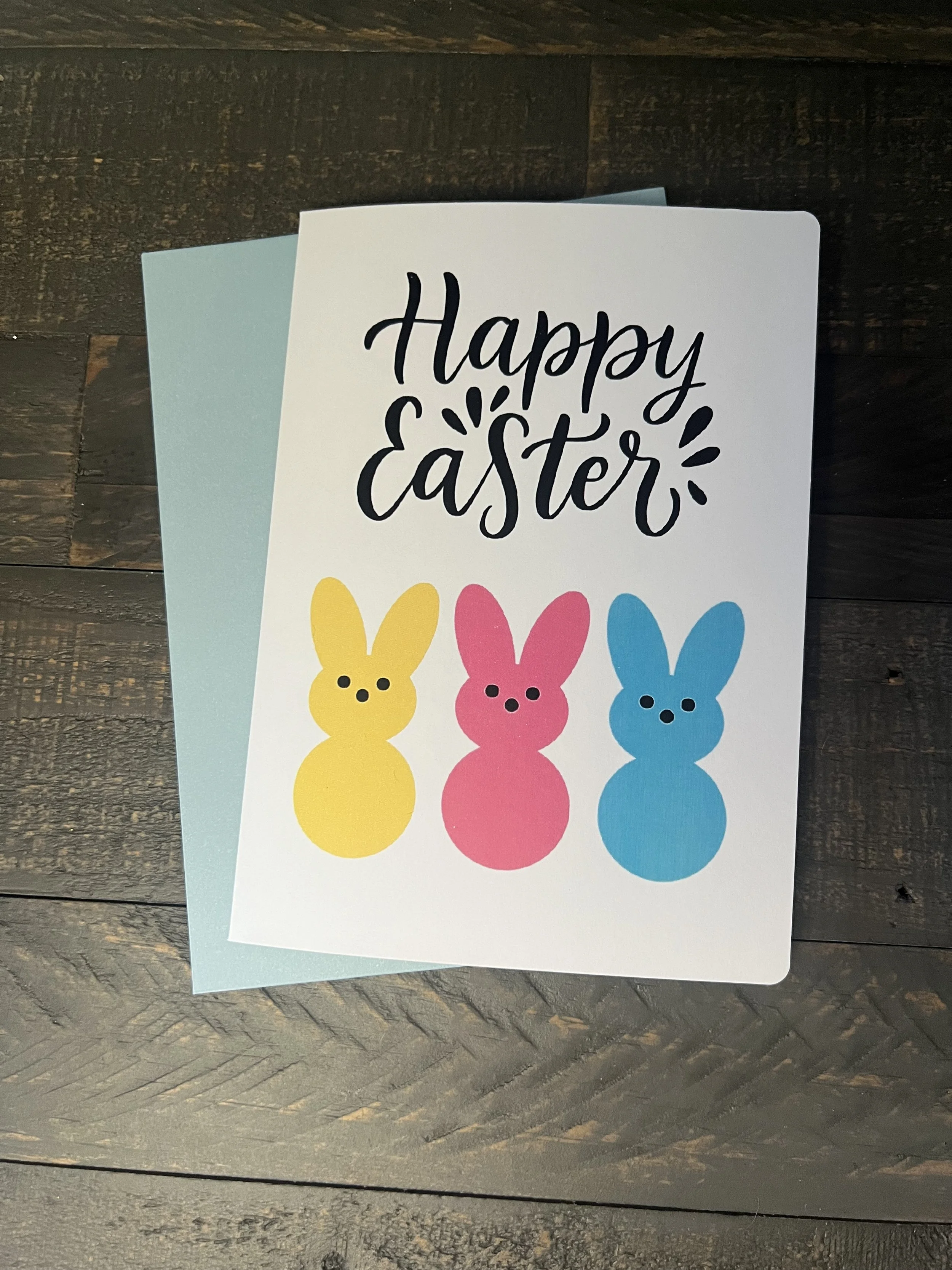 Happy Easter card with colorful bunny silhouettes and playful script on rustic wood background