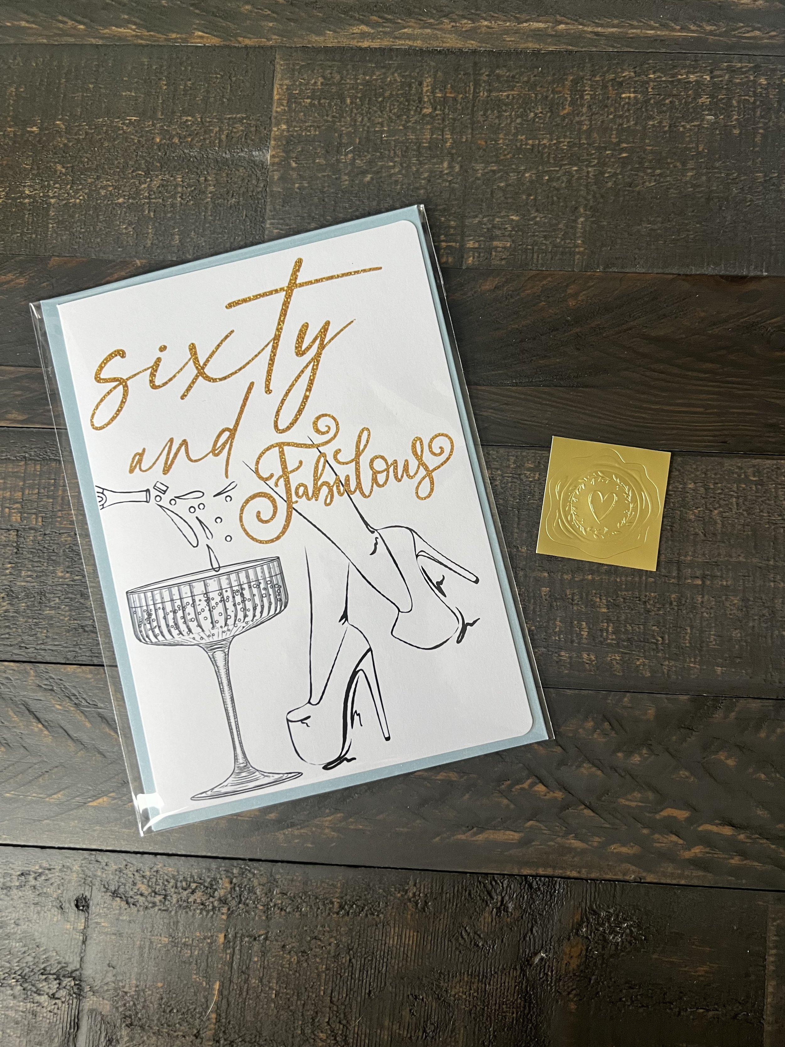 Styled flat lay of Sixty & Fabulous greeting card with coordinating envelope and gold wax seal style sticker.