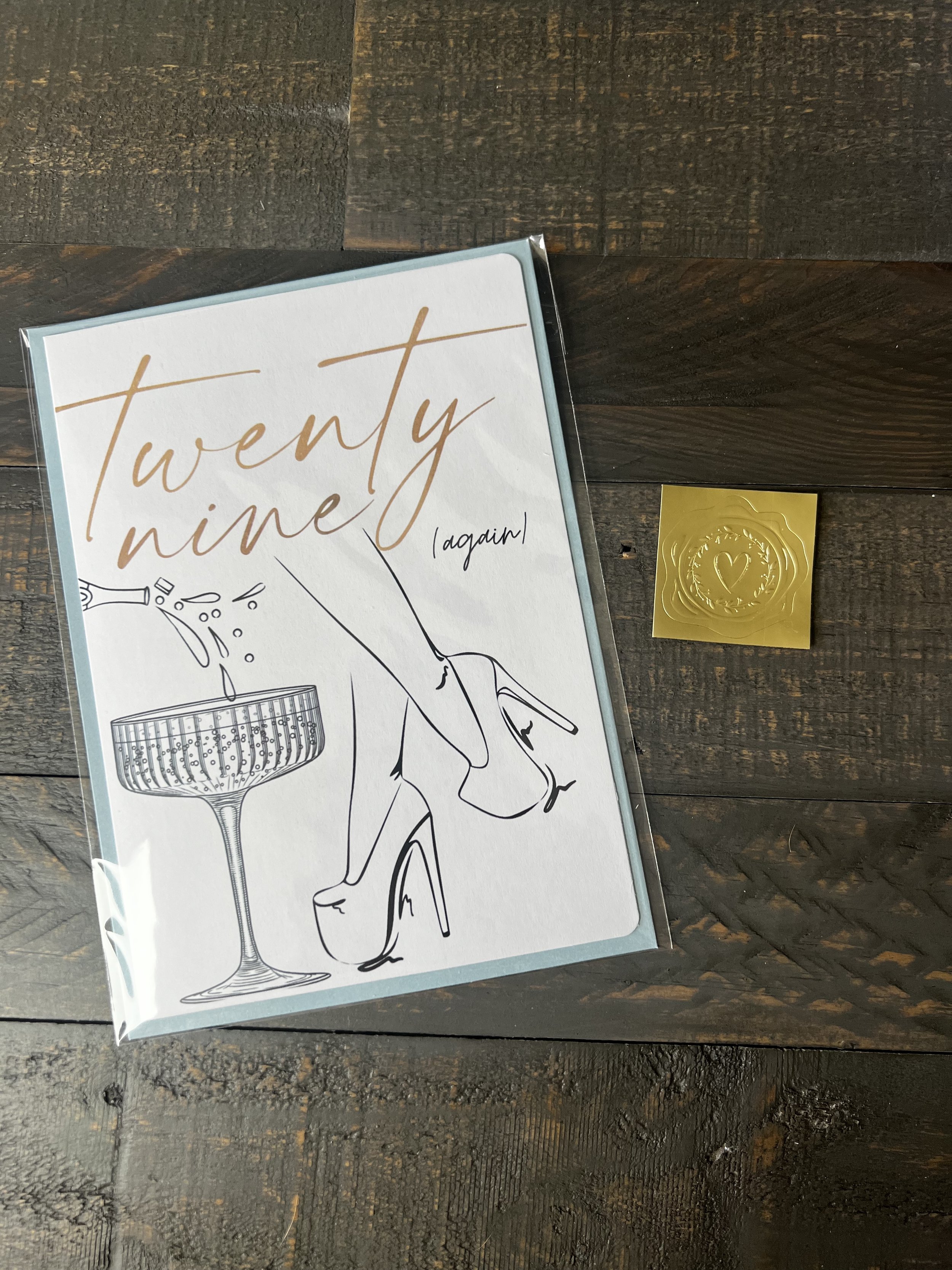 Styled flat lay of Twenty-Nine Again greeting card with coordinating envelope and gold wax seal style sticker.