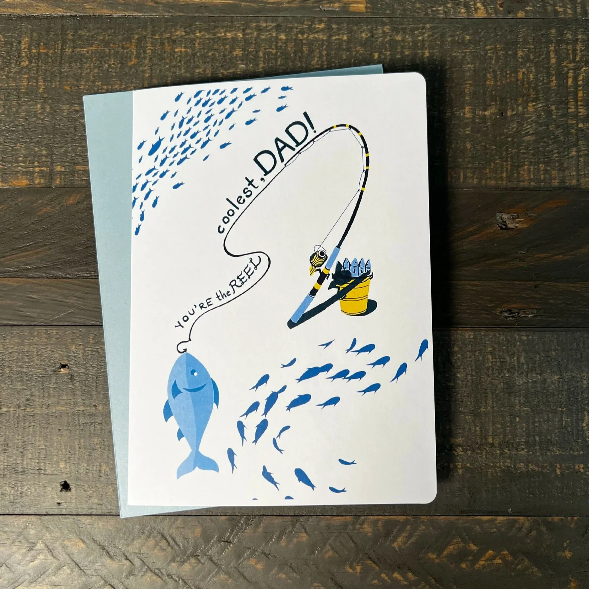 Fishing-themed Father’s Day card with fishing rod design and blue fish accents on wood background