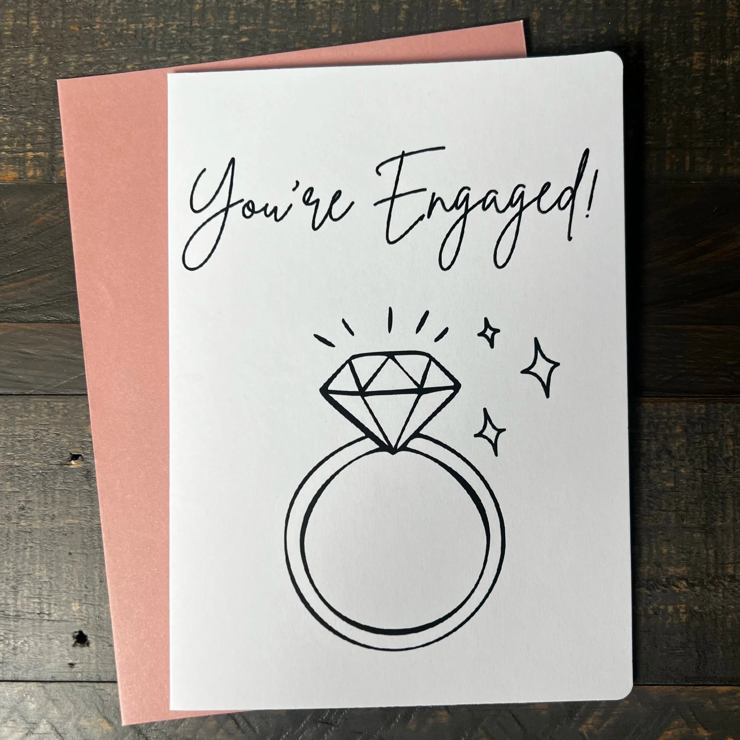 Front of You're Engaged! greeting card with coordinating blush pink envelope.