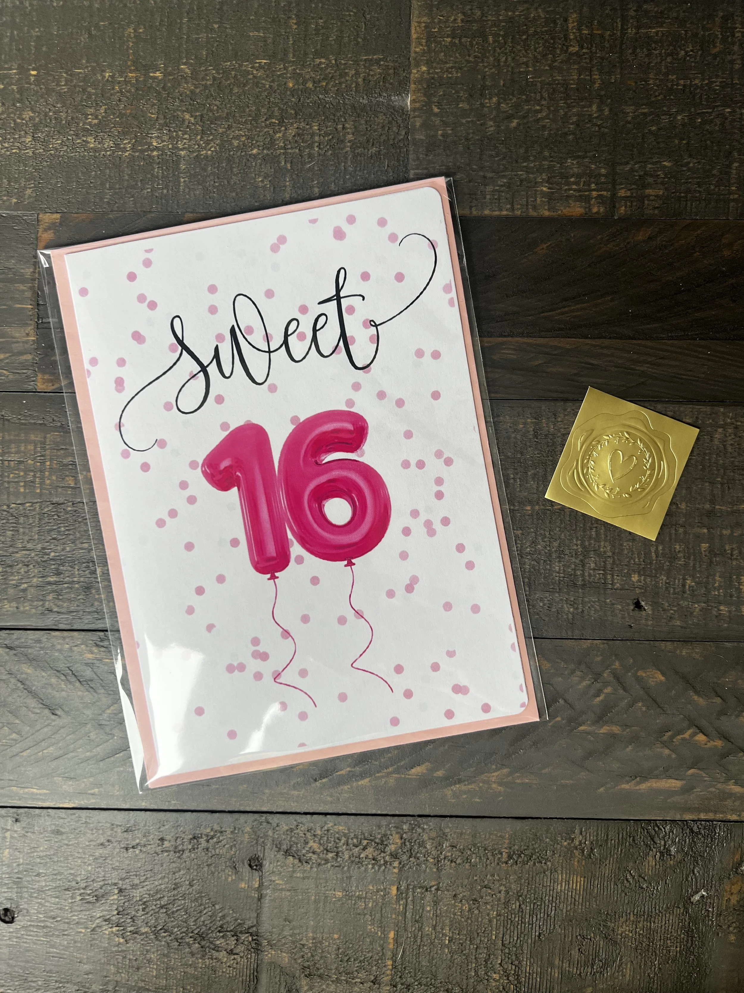 Styled flat lay of Sweetest Girl Birthday Card with coordinating pink envelope and gold wax seal style sticker.